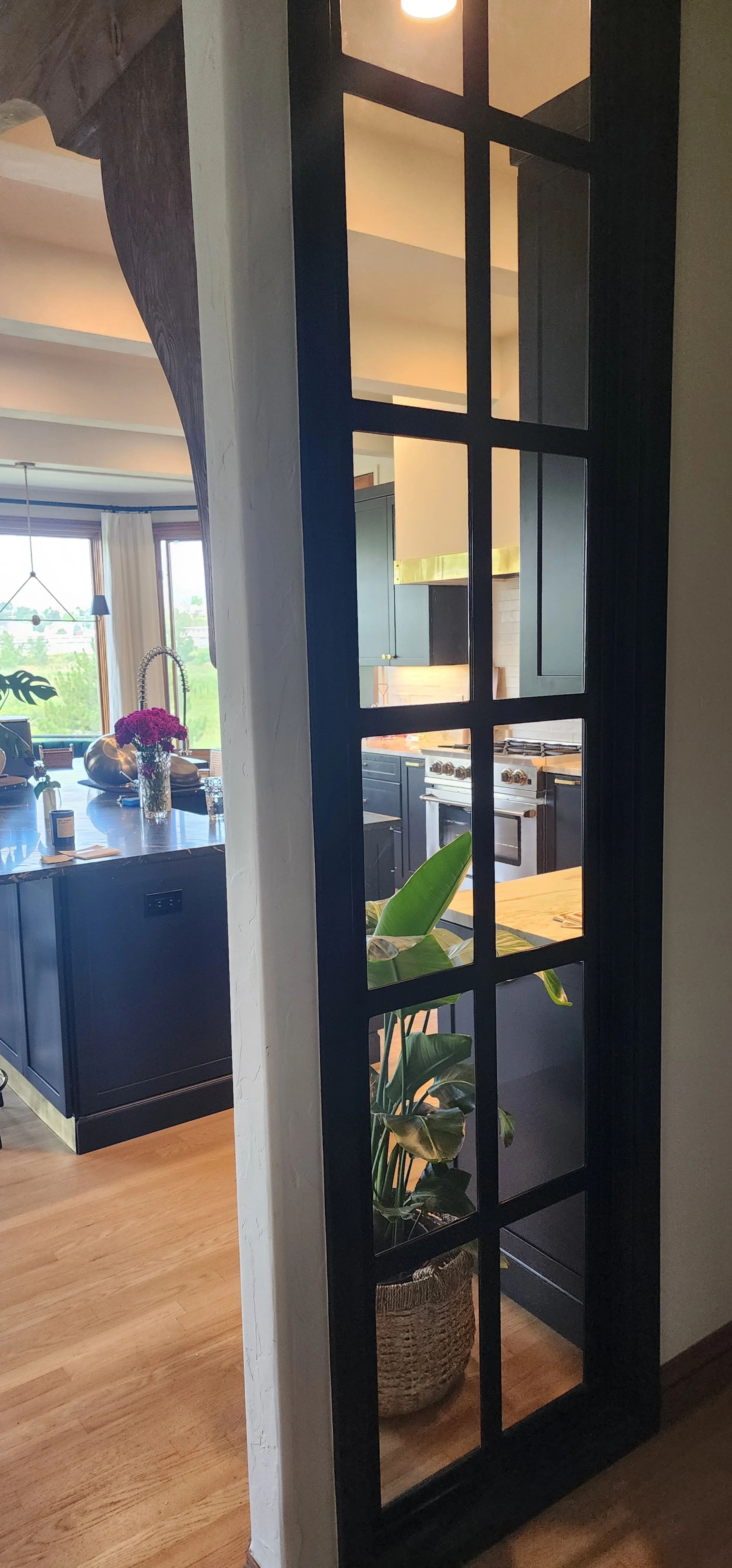 View into a modern kitchen through a sidelight, showing the Tri-horn Black kitchen cabinet, a stainless-steel stove, and stone counter tops.