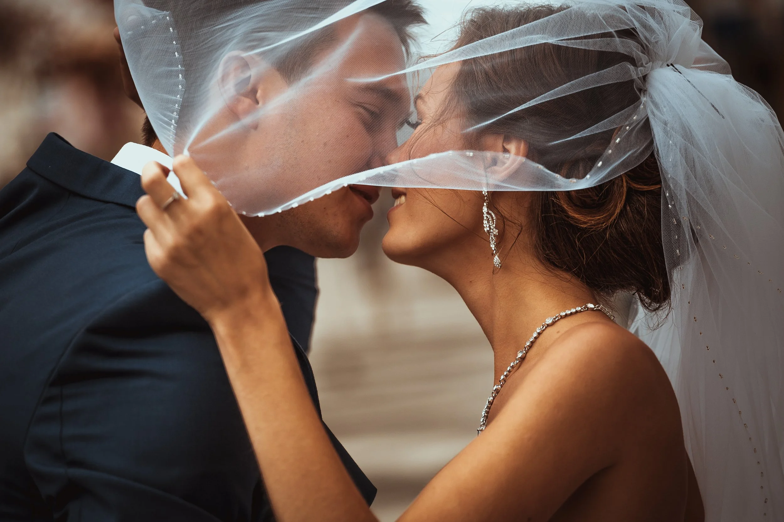 A bride and groom with closed eyes, close together under a wedding veil, sharing a tender moment.