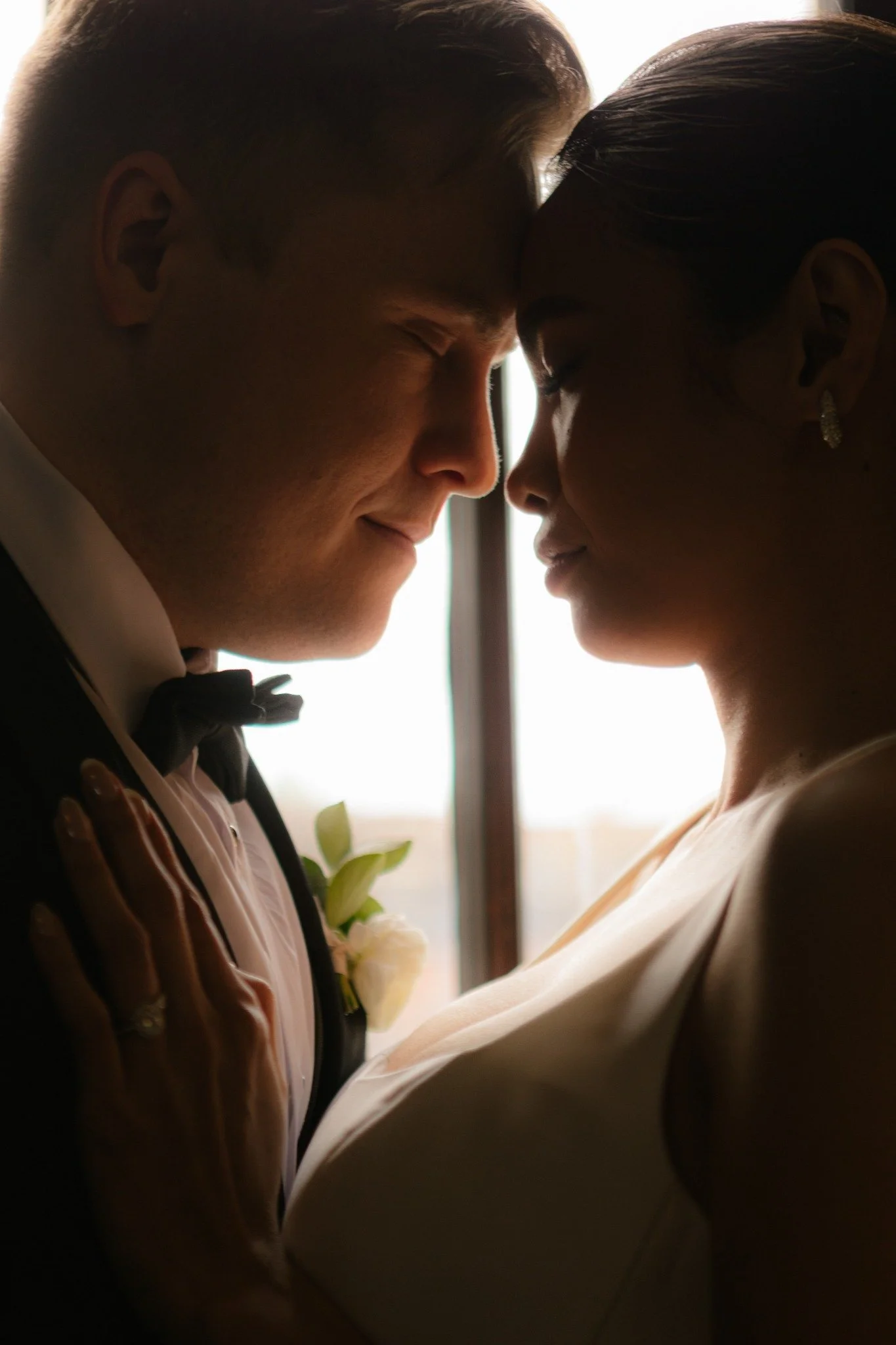 A bride and groom face each other with foreheads touching in a close-up silhouette on their wedding day.
