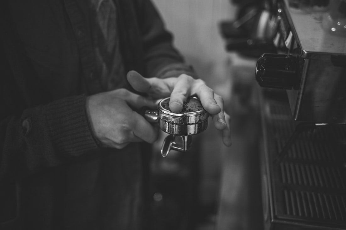 A barista smooths espresso in a portafilter standing in front of an espresso machine