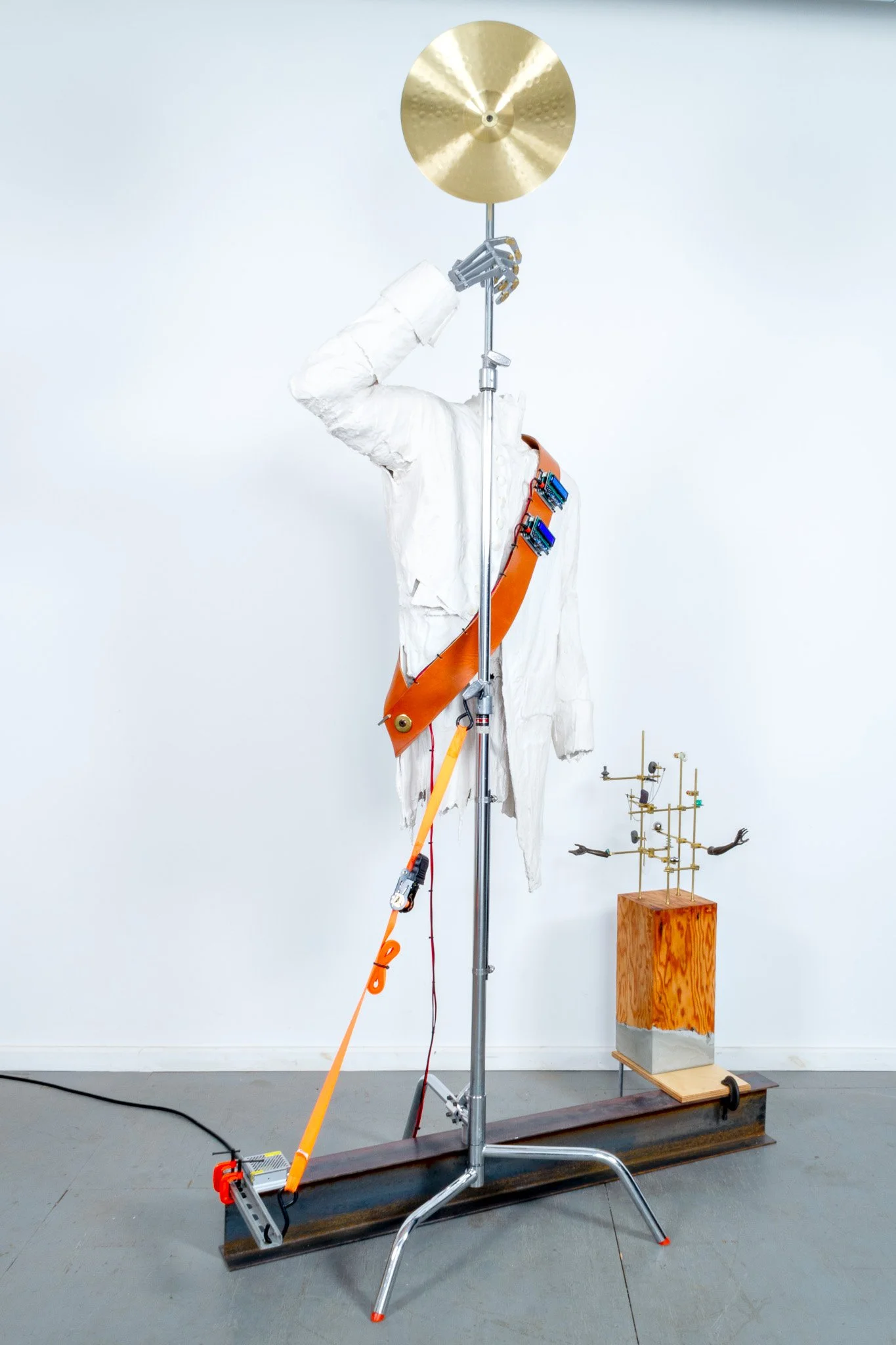   Apparition with Omens and Small Array,  2025  99” x 55” x 26  Gypsum cement, cardboard, gauze, replica frock coat, leather, electrical and electronic components, salvaged plywood, mortar, aluminum, brass, steel, ratchet strap, C-clamps, cymbal, sto