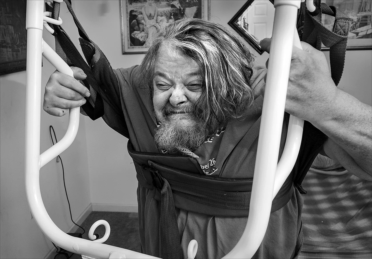 February 2017: Mark relies on a lift for even basic things like maneuvering on and off of the toilet. “I have a sit and stand lift that allows my personal assistants to lift me up and set me on my wheelchair, in my recliner, or to put me on or take me off the toilet.” Mark says not having the lift would mean the fire department would have to come to pick him up even if he needed to adjust his position in bed. “I call my sit and stand ’Sarah’ because she is the love of my life and without her my life would be really devastating. You know, not being able to get out of bed, I couldn’t live like that.”