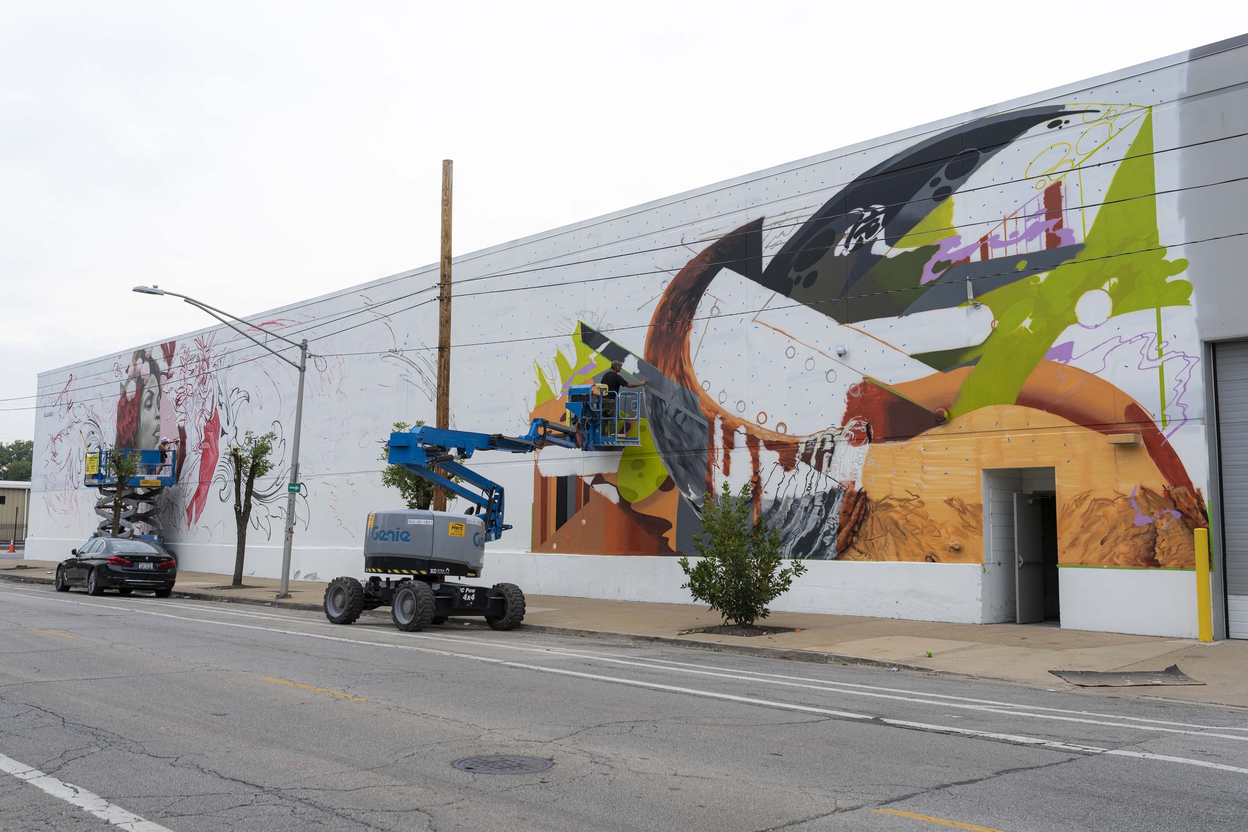 Street mural in progress with lift equipment and painter on a building wall