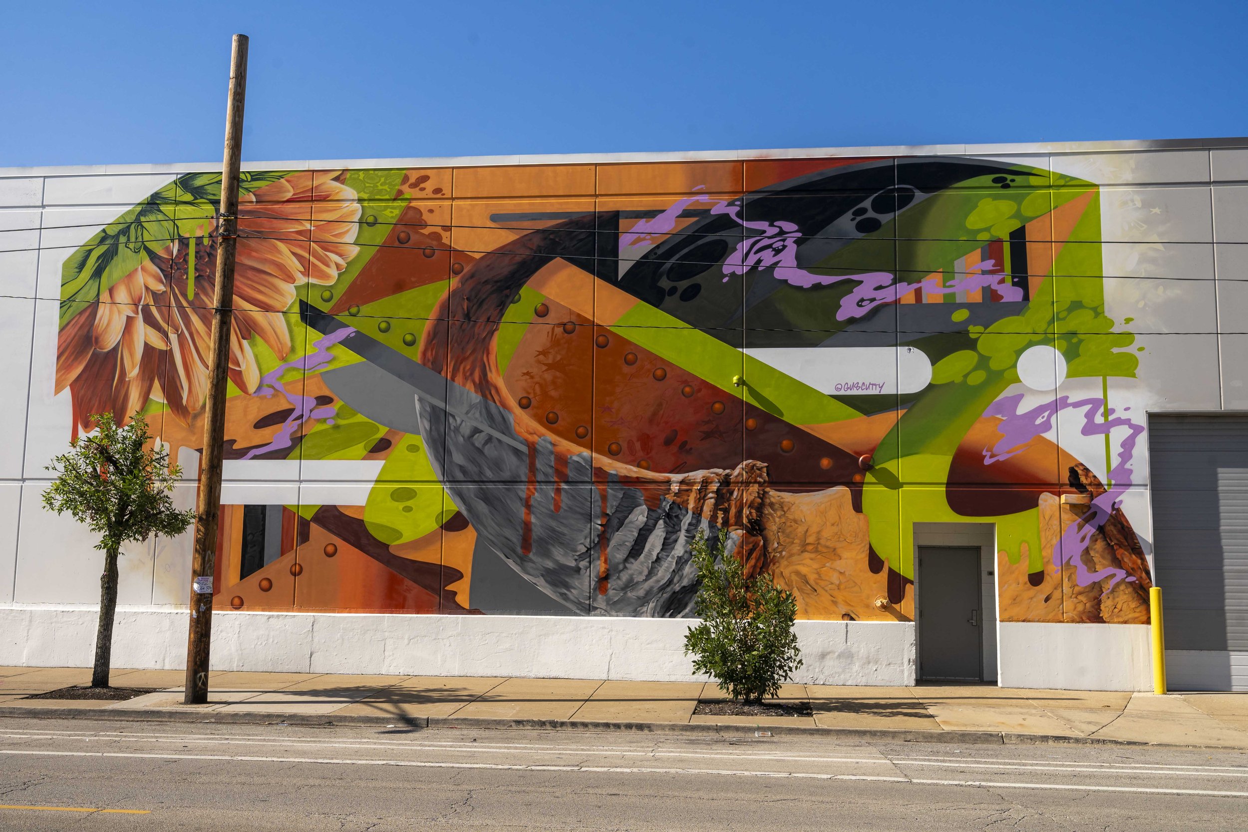 Colorful abstract mural on a building wall featuring geometric shapes, a large flower, and dynamic brush strokes in orange, green, and purple hues.