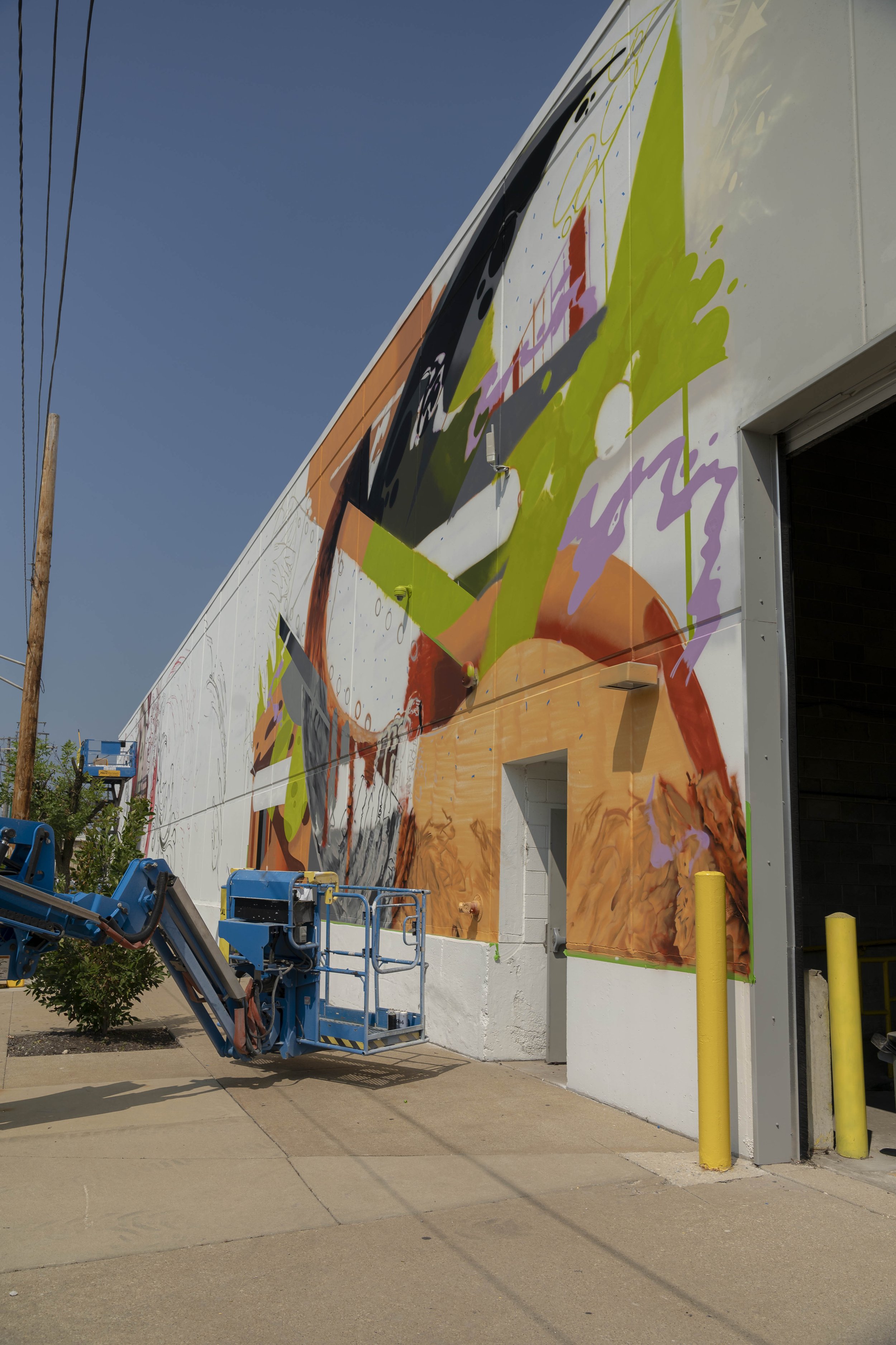 A large, colorful mural on the side of a building, with a boom lift parked nearby.