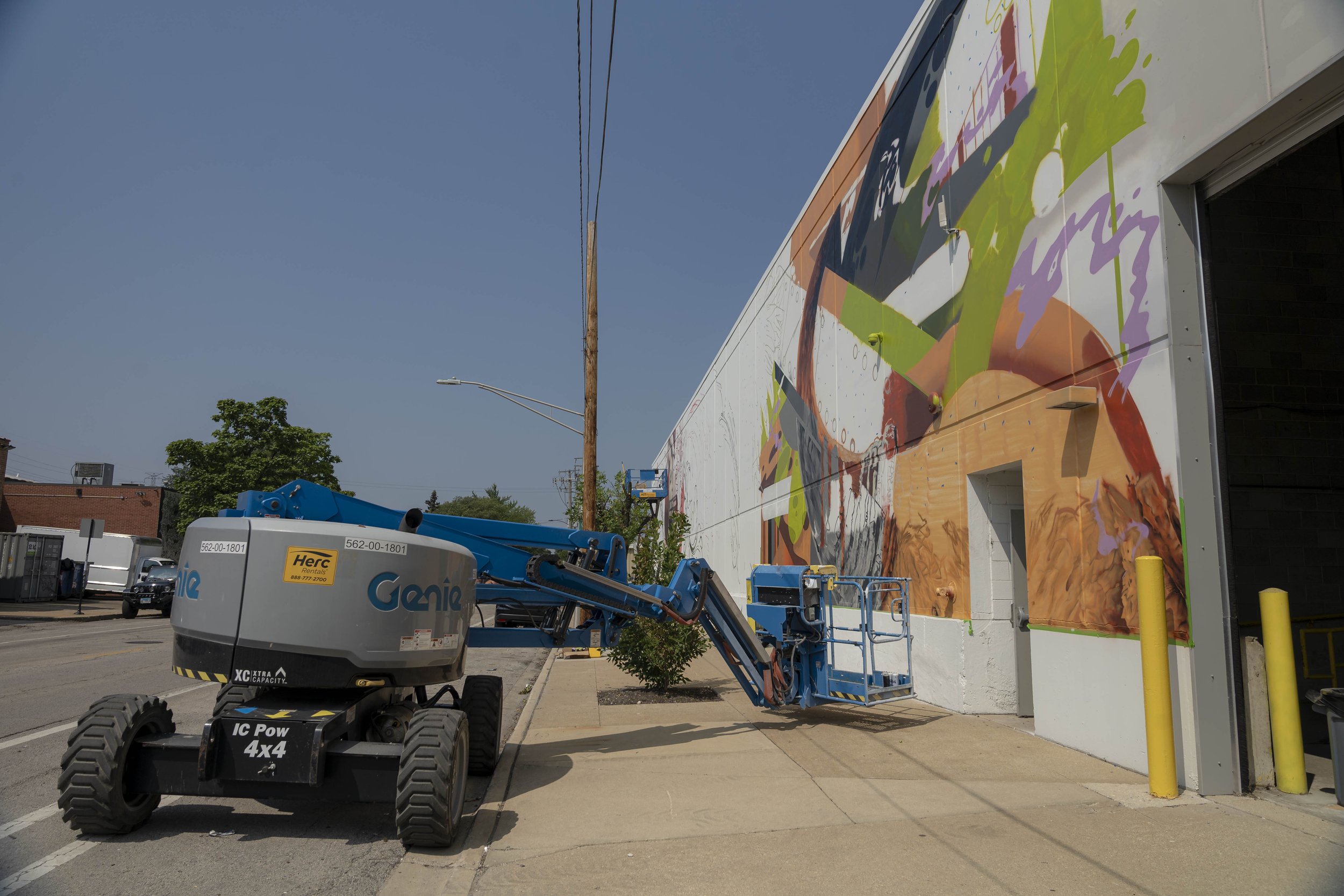 A boom lift near a colorful mural on a building wall.