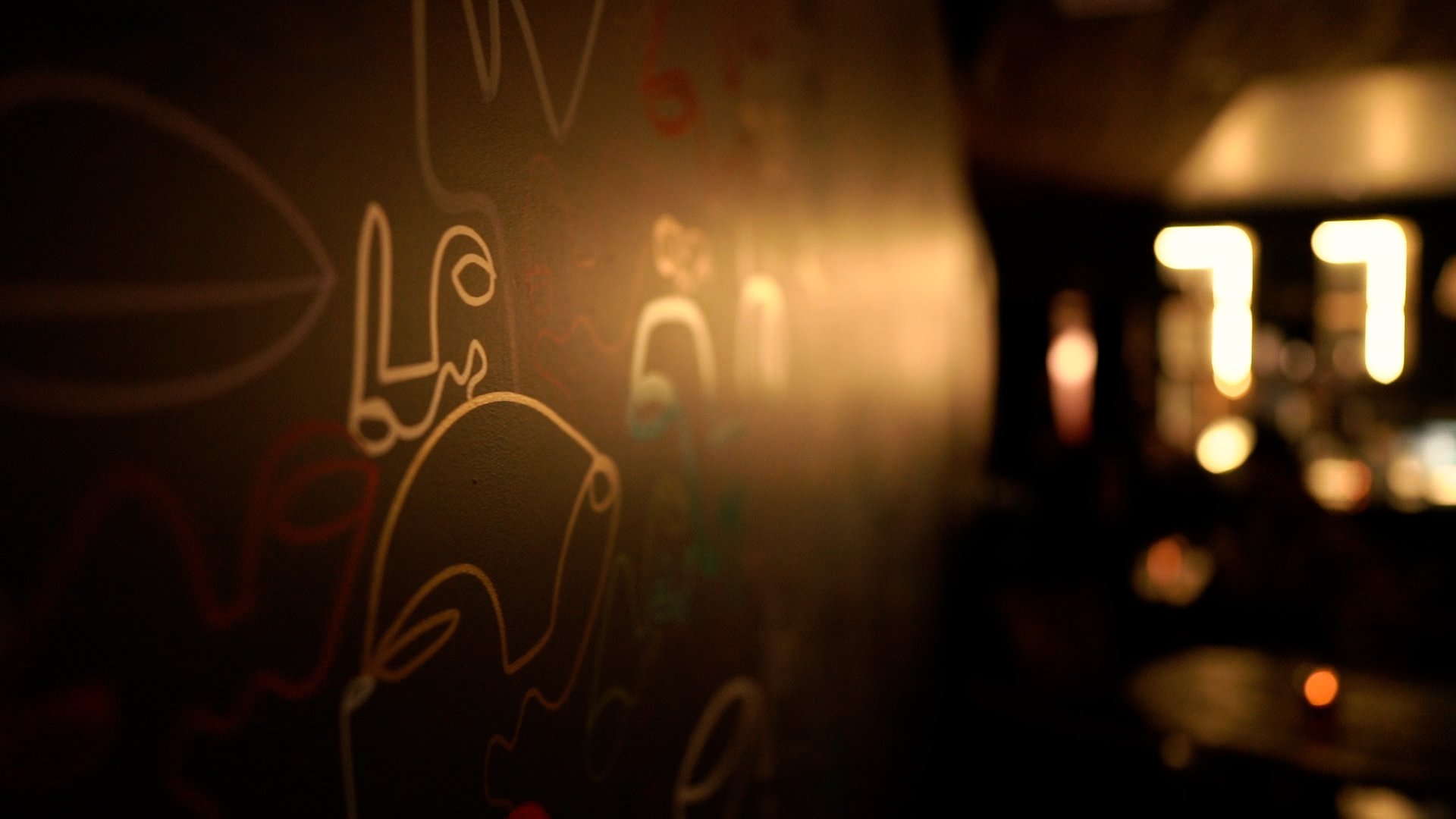 Abstract line art on a dimly lit wall with blurred lights in the background.