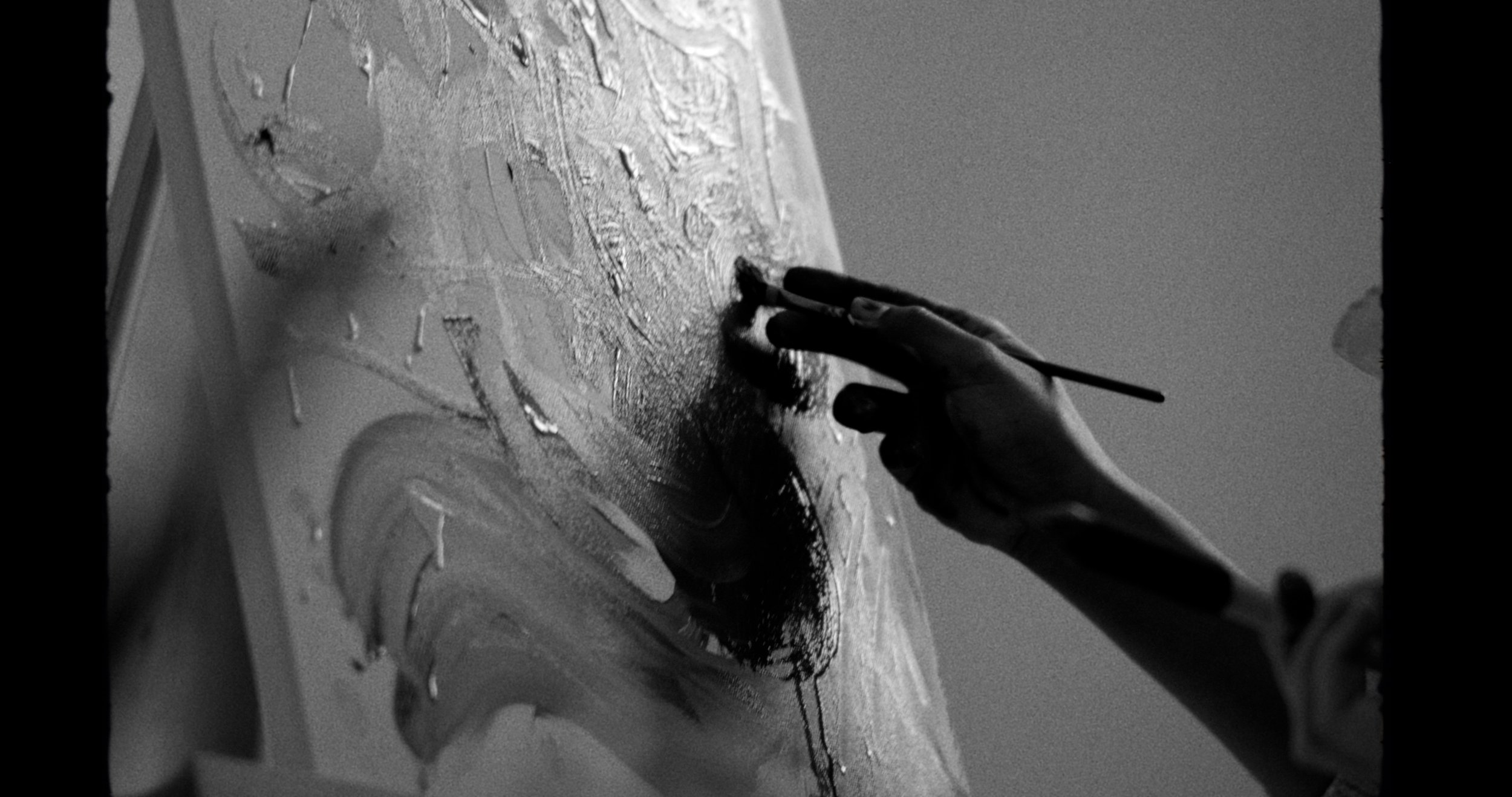 Black and white image of a hand painting on a canvas, focusing on the fingers applying paint.