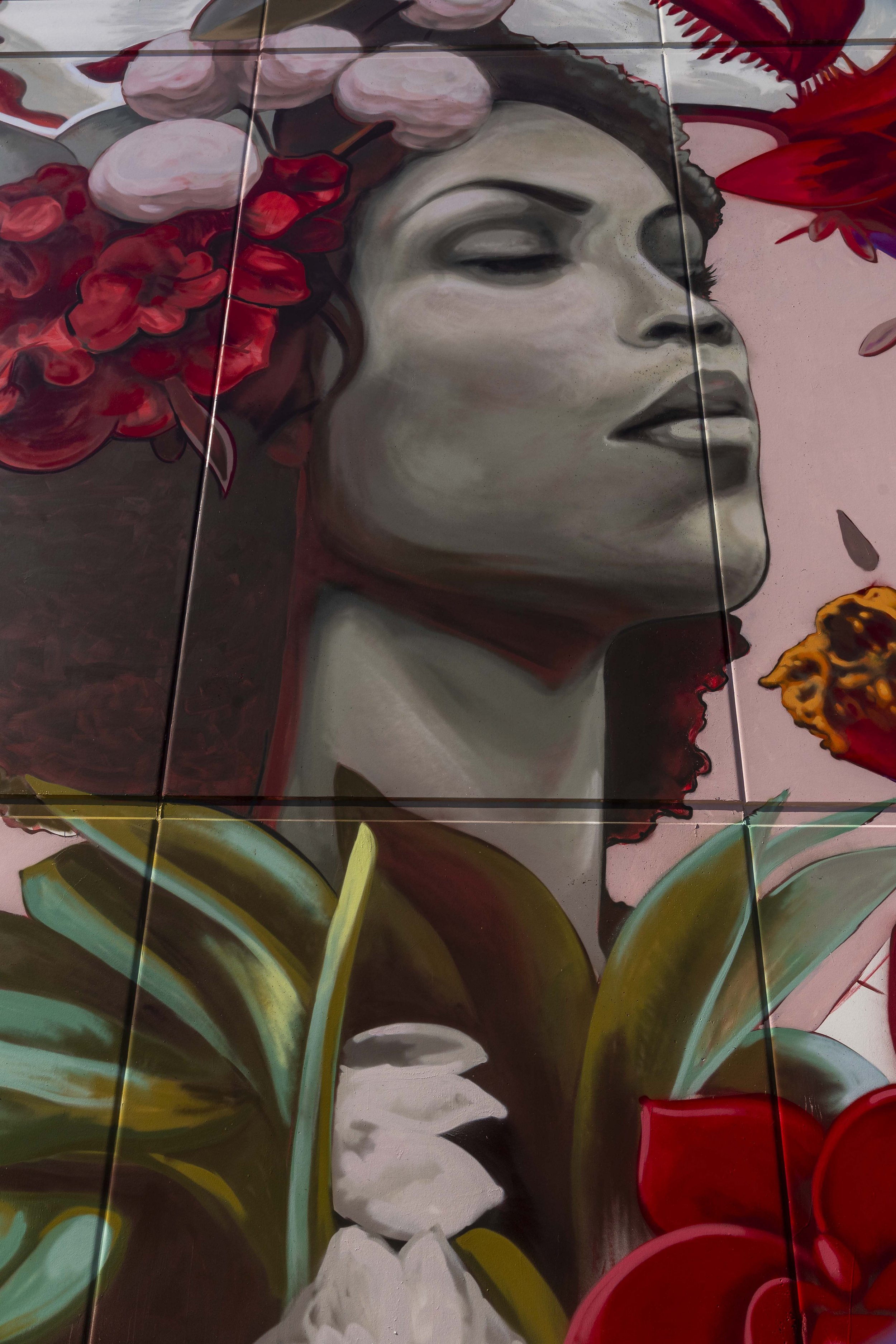 Street art mural featuring a woman's profile with closed eyes, surrounded by vibrant red and white flowers.