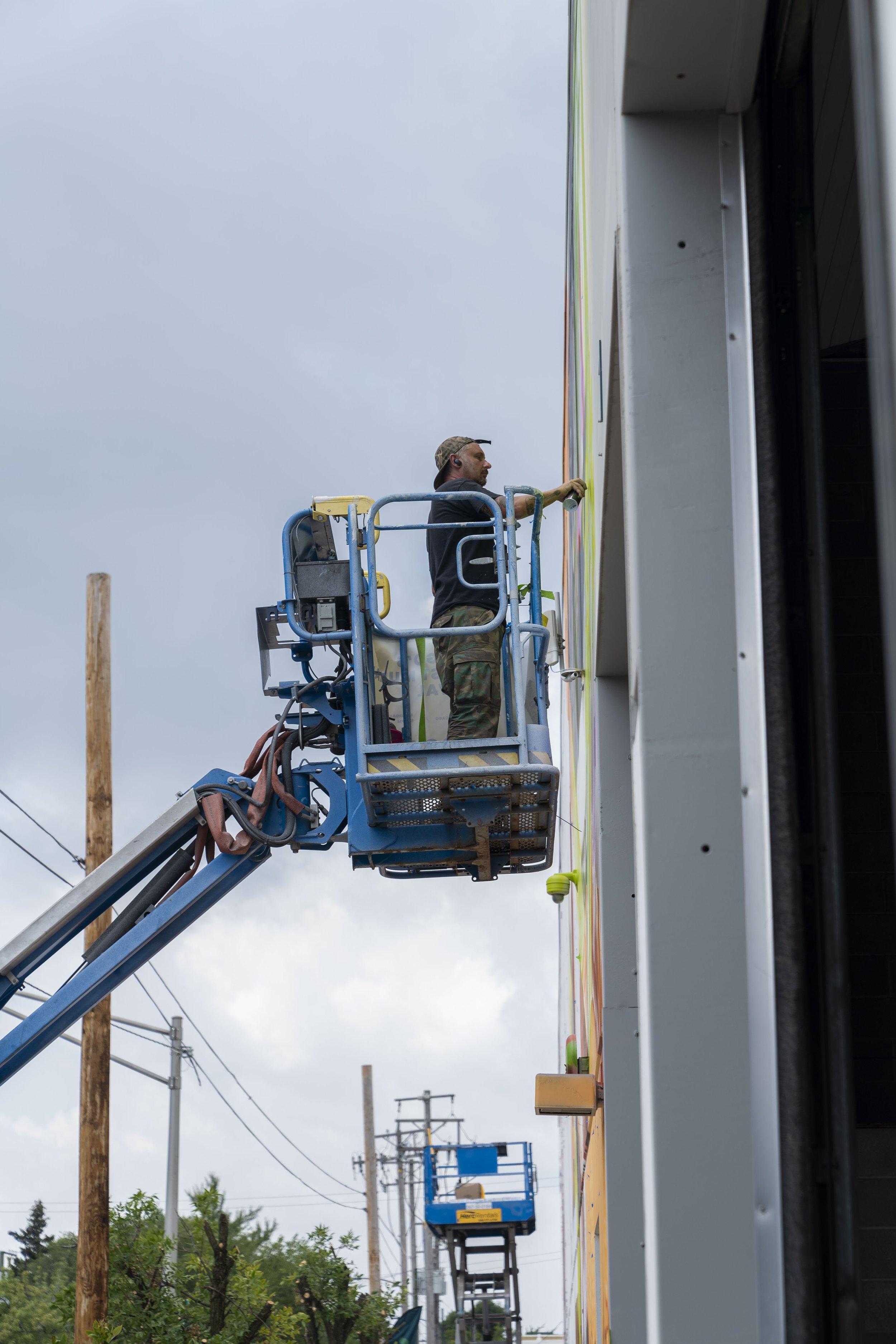 Person on a blue cherry picker painting a wall.