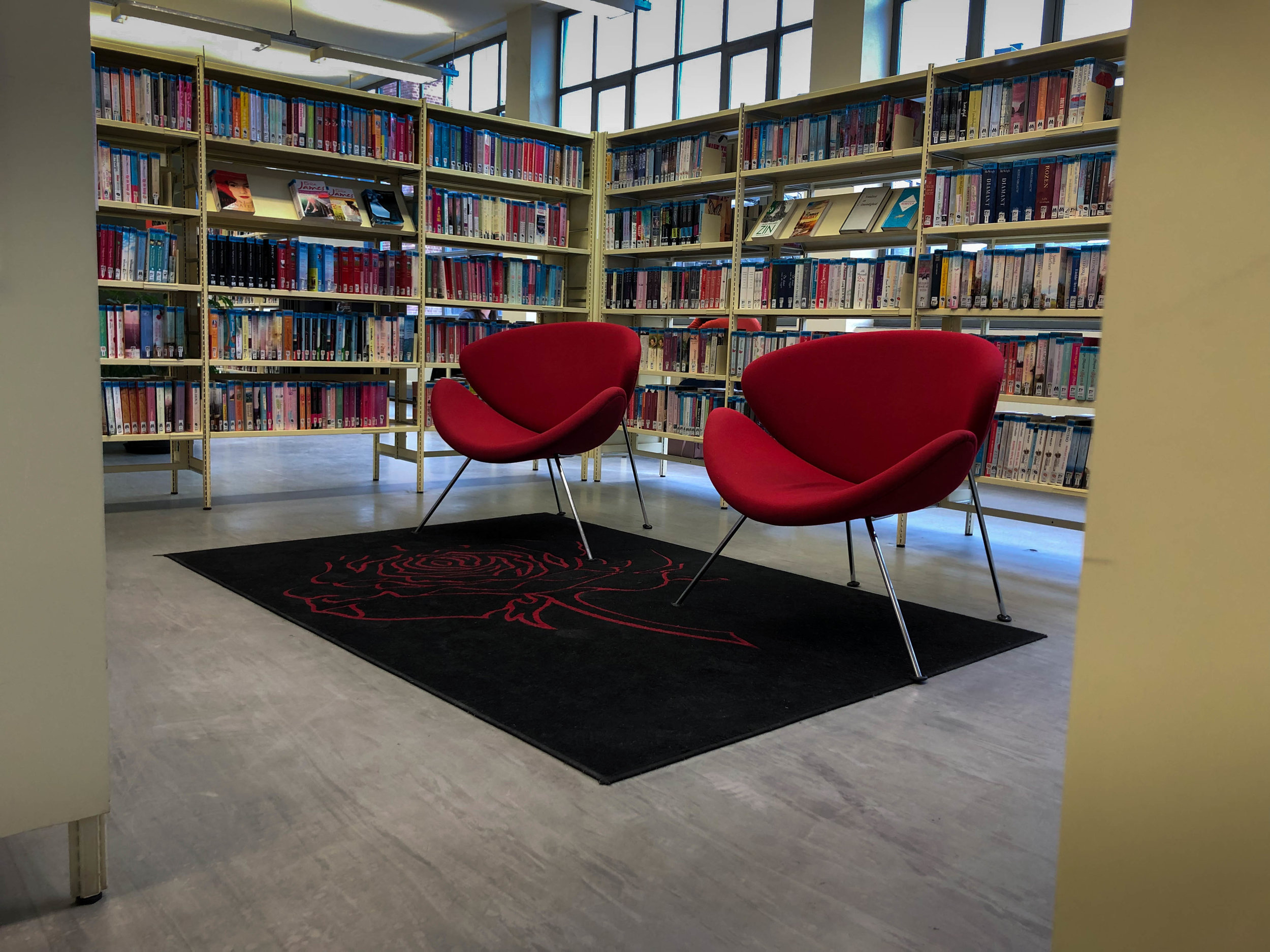 Library in Leuven, 2 red sofas surrounded by shelves stacked with books.