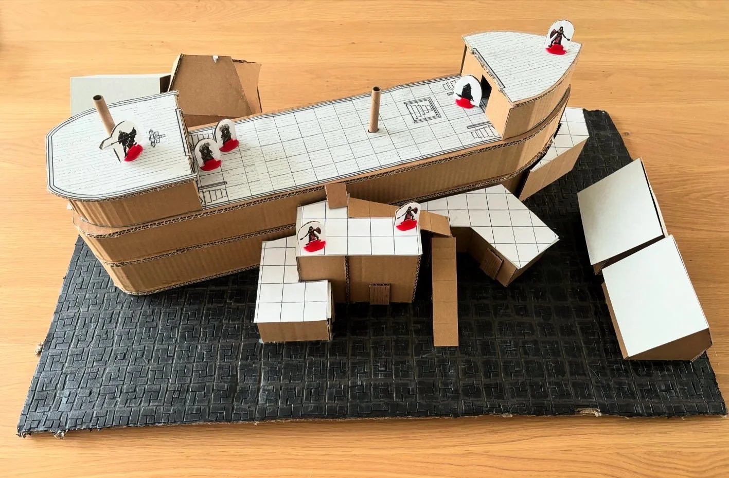 D&D scenario terrein voor de Vergiftigde Poseidon, uit karton, gestrand schip waar doorheen de jaren tegenaan gebouwd is, culteleden staan op de dekken van het schip.