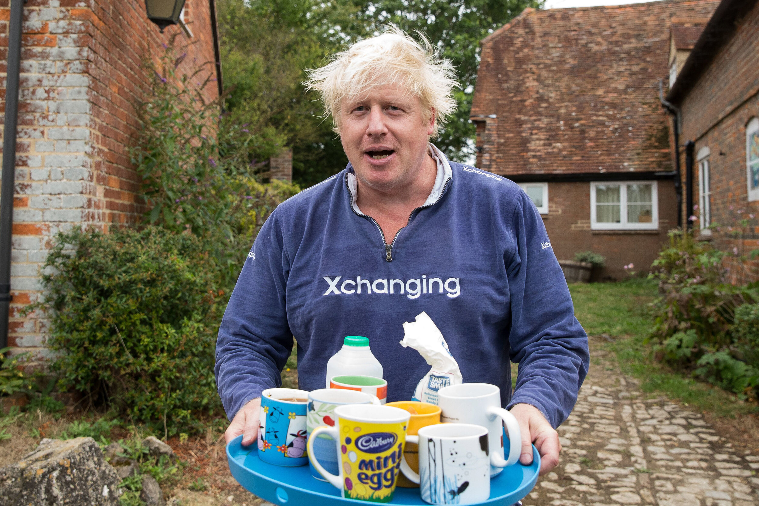  Boris Johnson brings tea for the press to drink outside his house in Thame. Picture by: Aaron Chown/PA Images. Date taken: 12-Aug-2018 