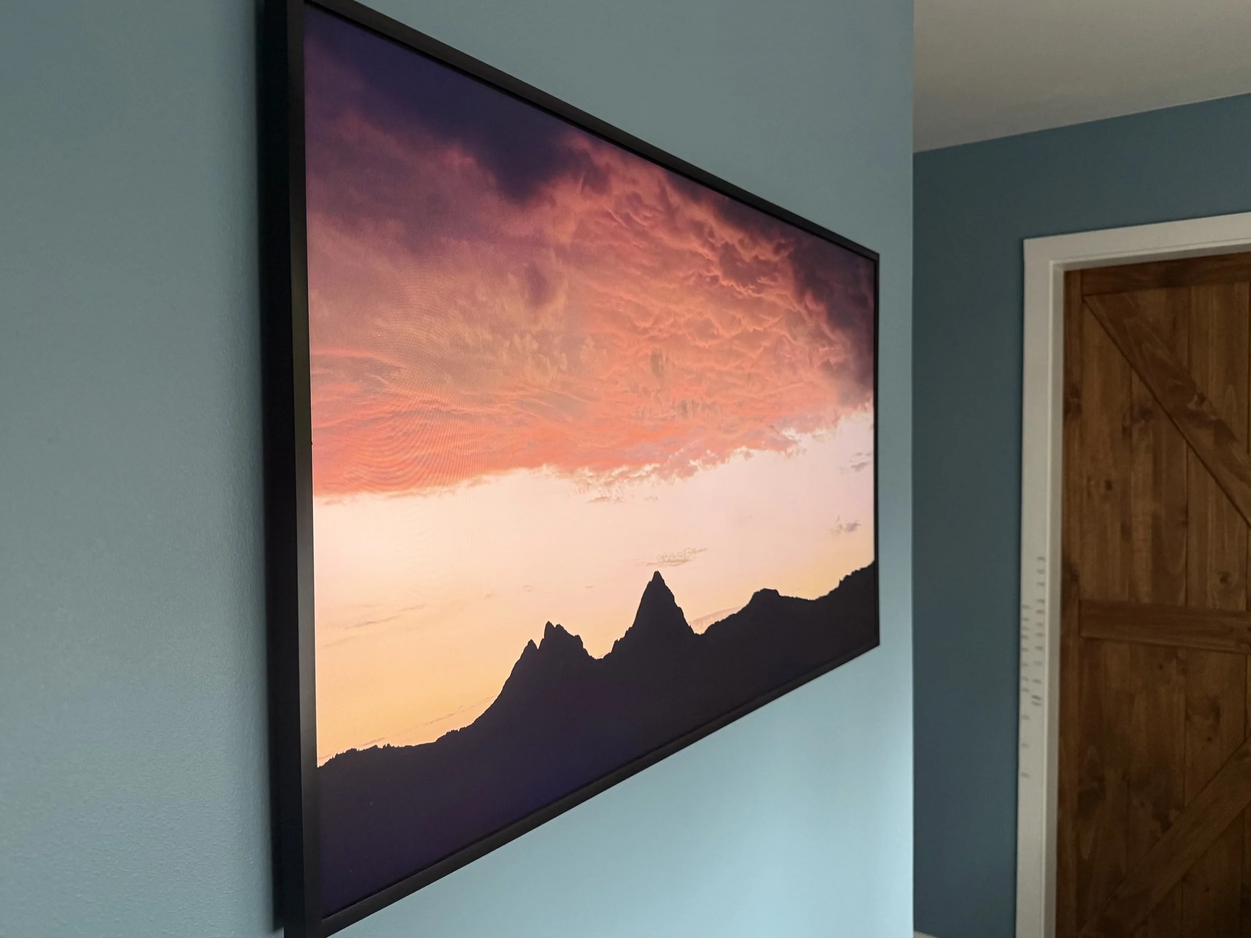 Sunrise over mountains in switzerland image displayed on FrameTV with blue walls around it and a door frame with kid heights marked along it in the background.