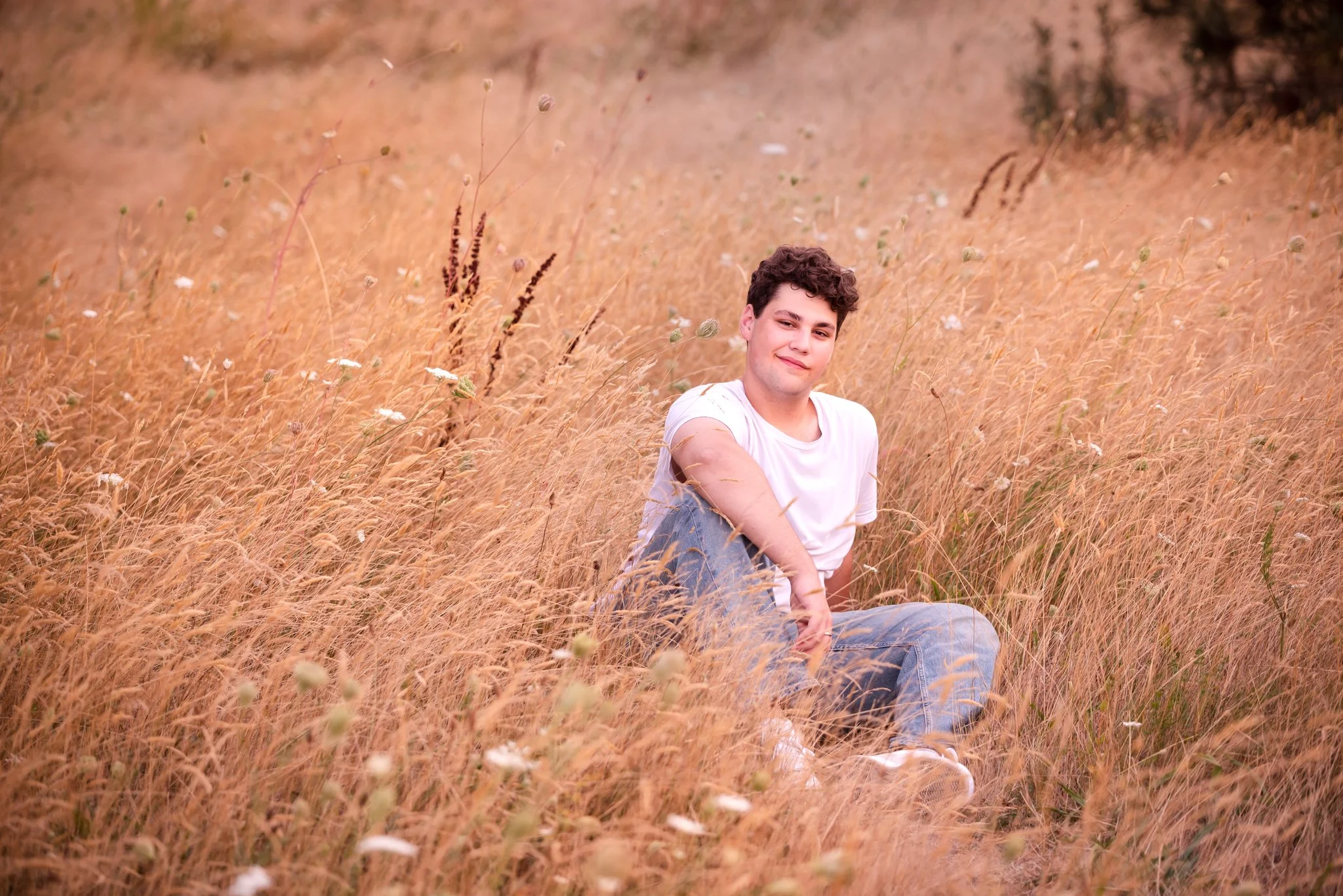 Senior boy in white t-shirt and jeans sitting in golden grass in the gardens at the University of Washington in Seattle, WA