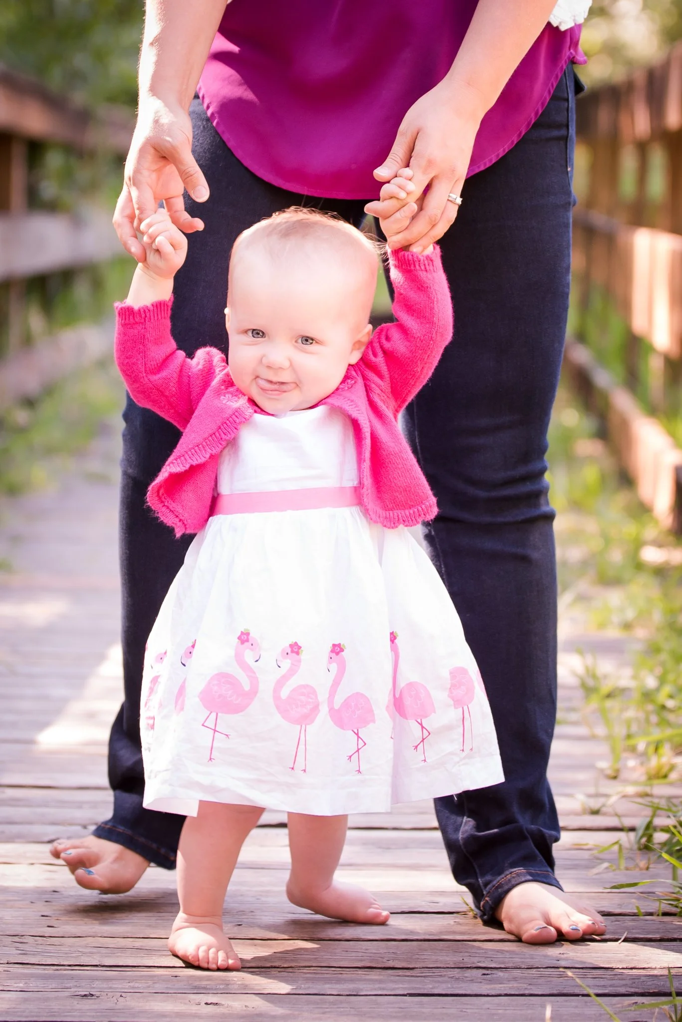 one year old girl birthday photos in pink flamingo dress walking with tongue sticking out