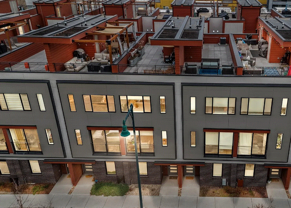 View of rooftop patio spaces on an apartment building, featuring outdoor furniture, grills, and a pergola, with a streetlamp in the foreground.