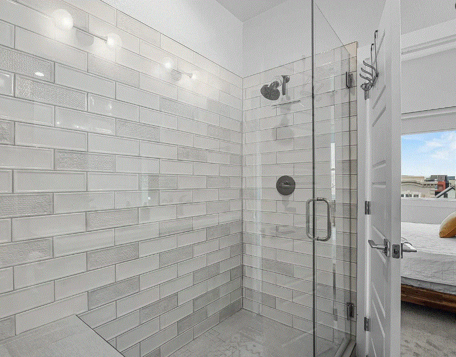 A modern walk-in shower with white subway tile walls, a glass door, and a mounted showerhead.