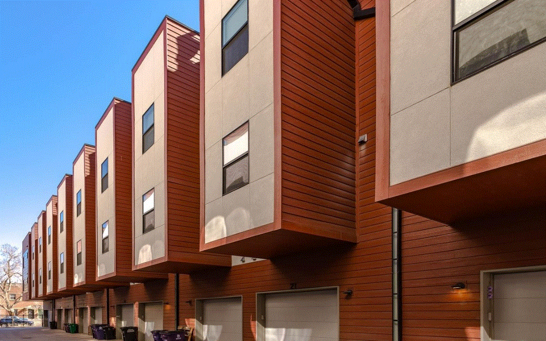 Modern multi-story apartment building with red and beige exterior and small overhanging balconies.