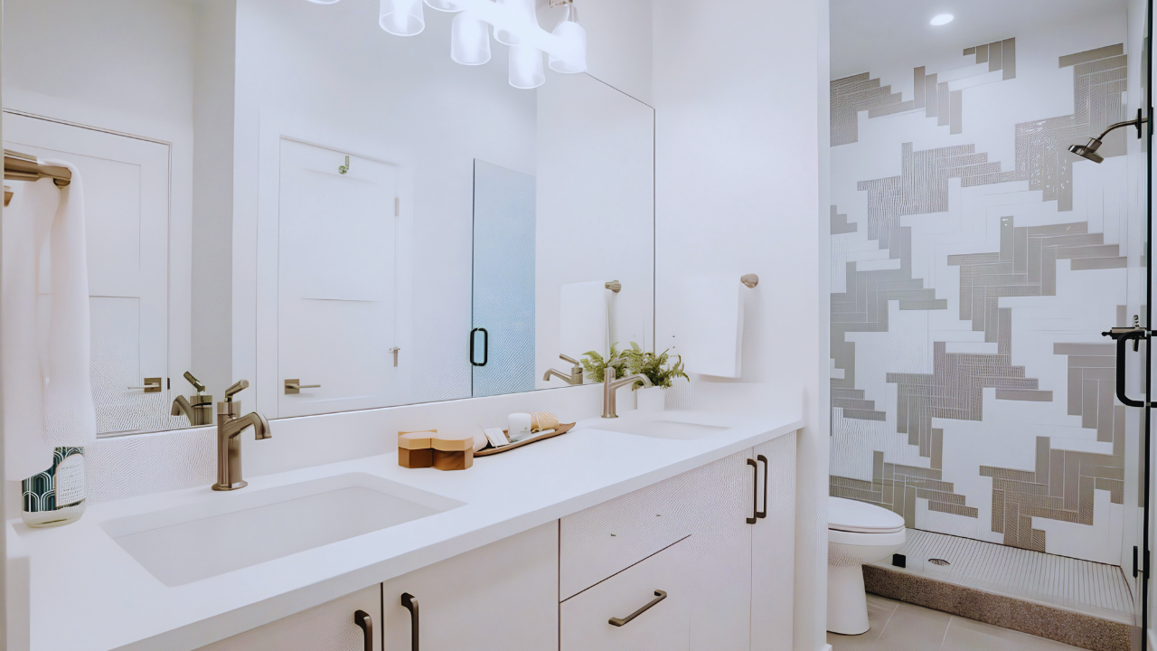 Modern bathroom with double vanity, large wall mirror, decorative wall art, plant, white towels, and a walk-in shower with patterned tiles.