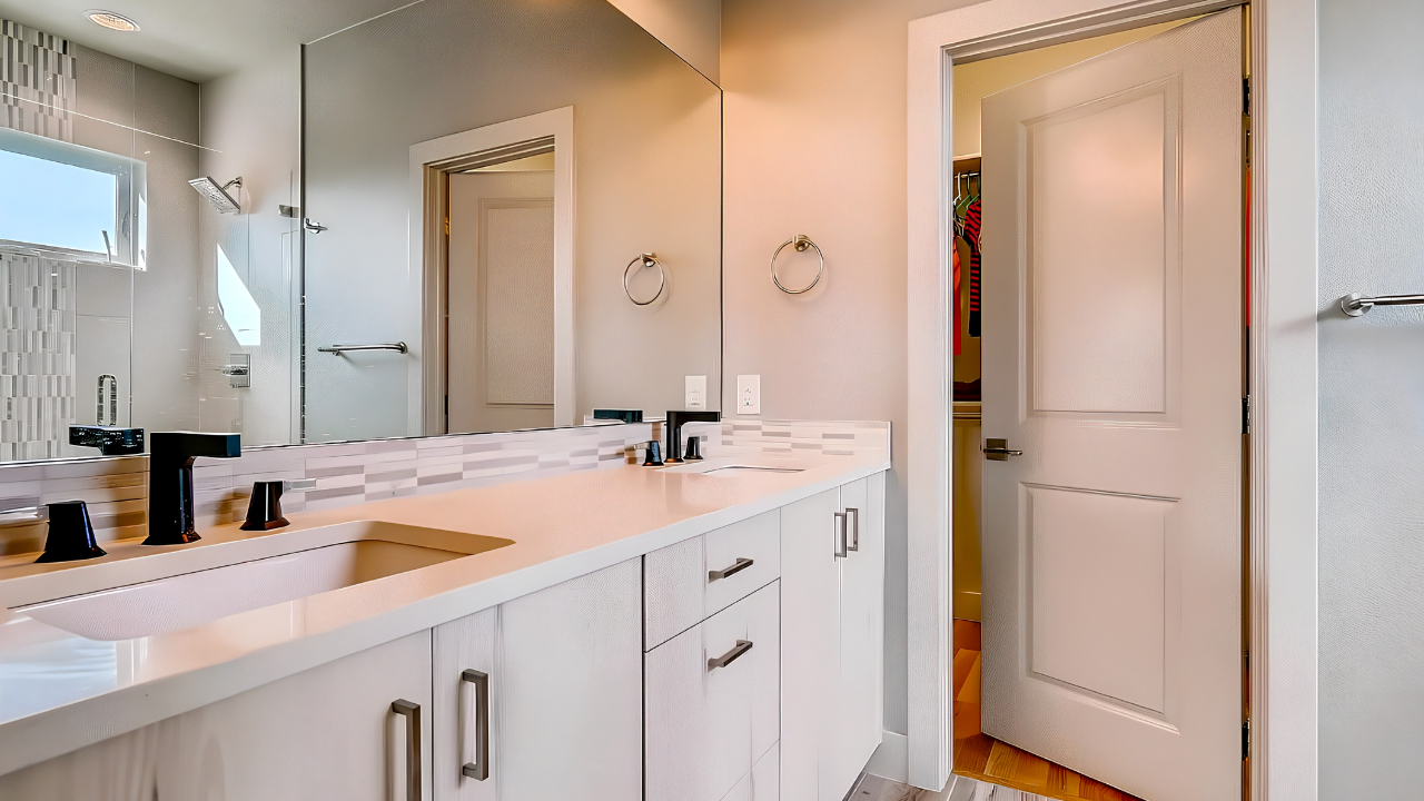Bathroom with white vanity, dual sinks, black fixtures, large mirror, towel rings, and a walk-in shower with glass door and tiled walls.