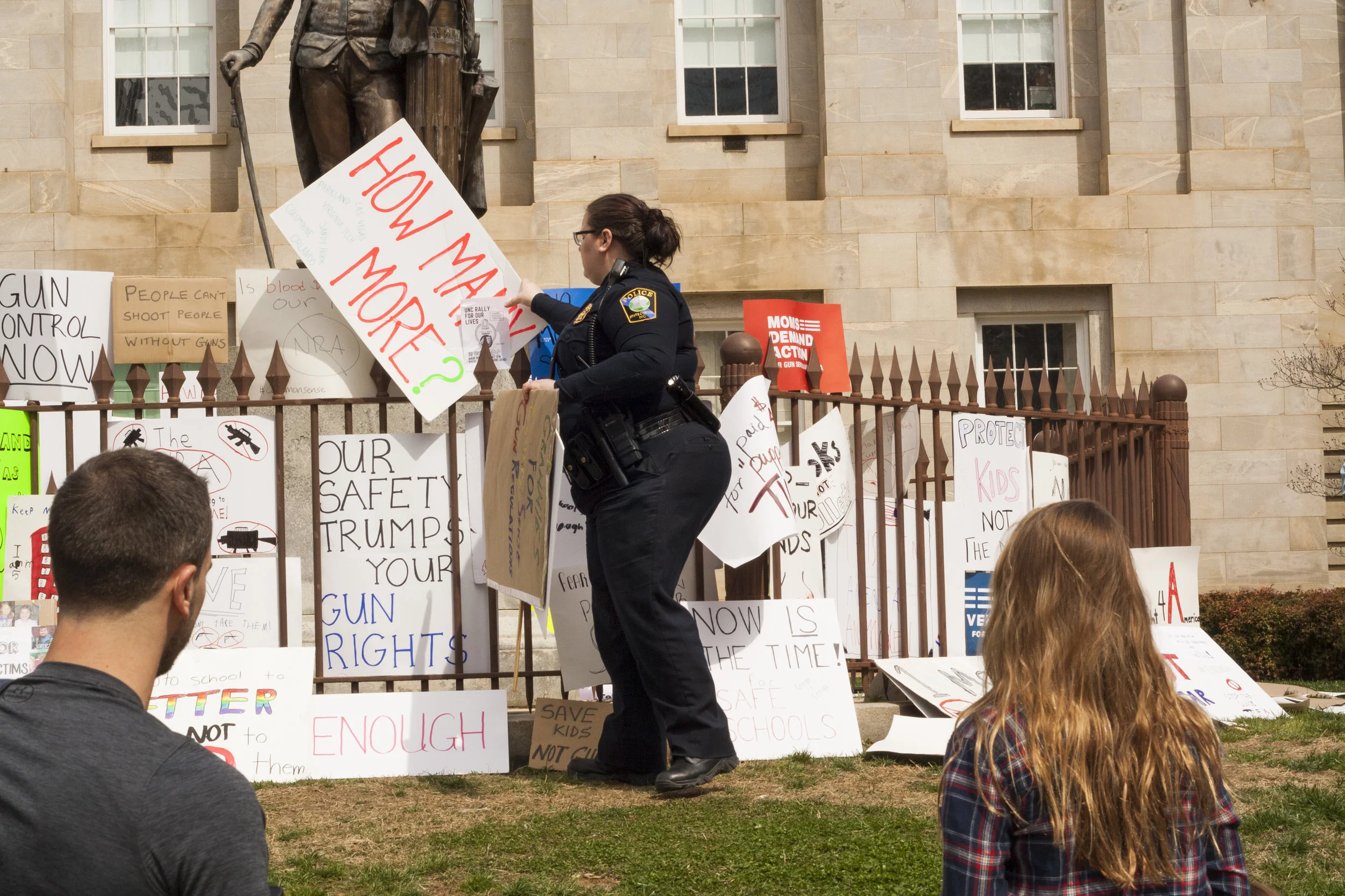 A police officer takes down signs saying it is litter as protesters observe.