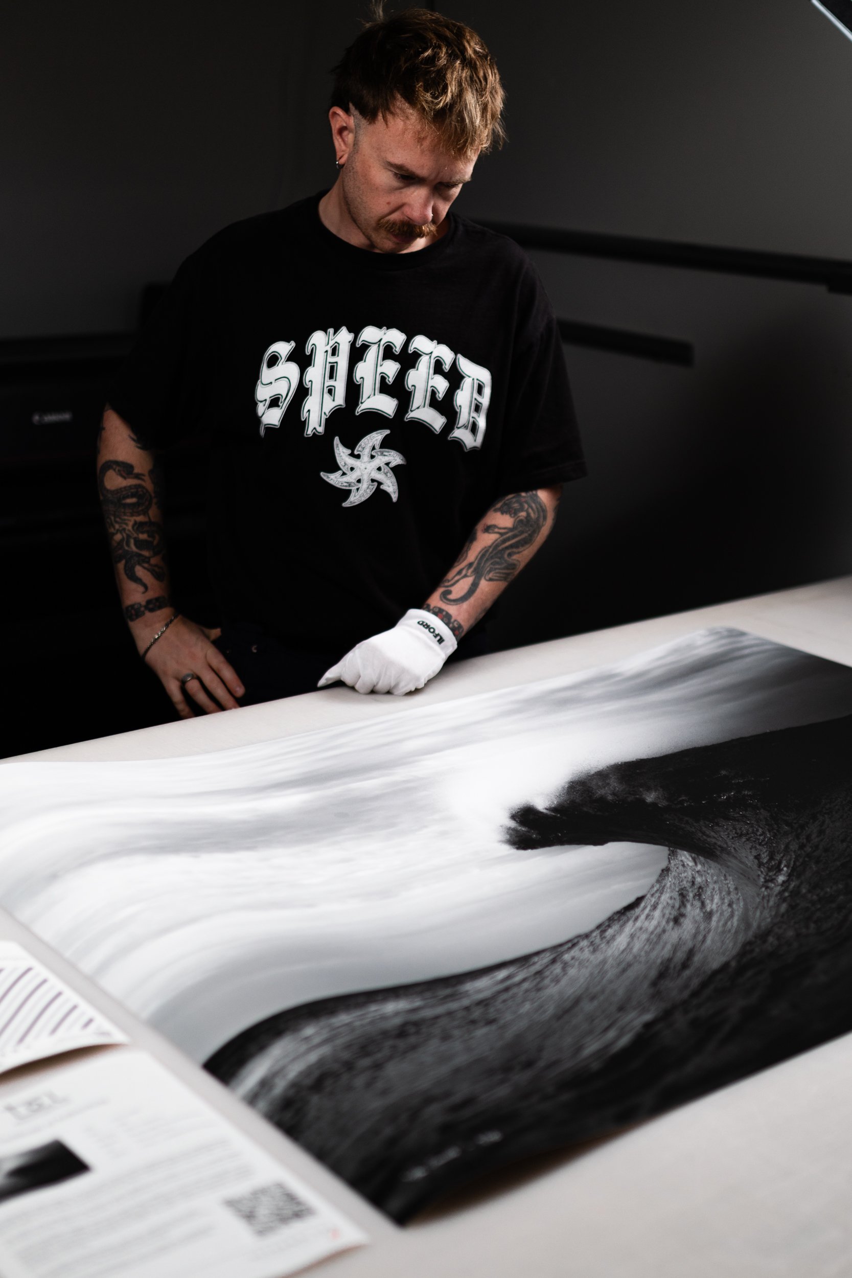 Ocean Photographer Tal Lemmens, wearing a white glove, inspecting a large black and white photograph of a wave on a table.