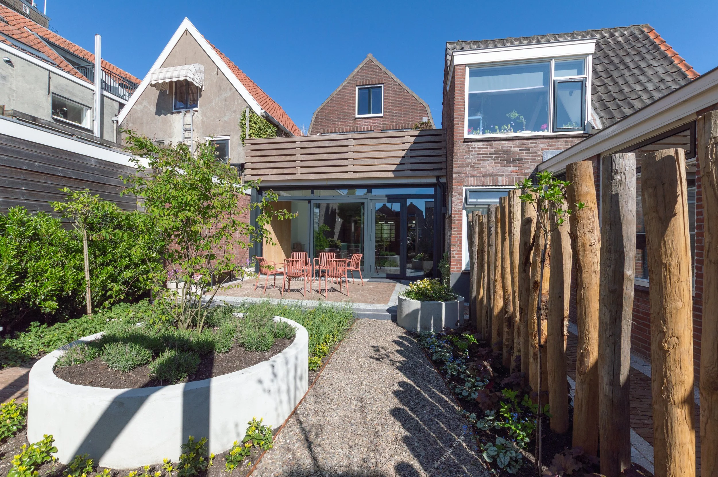 moderne binnentuin met houten palen en betonnen bak, grind, planten en bestrating. Moderne achterpui in binnenstad.