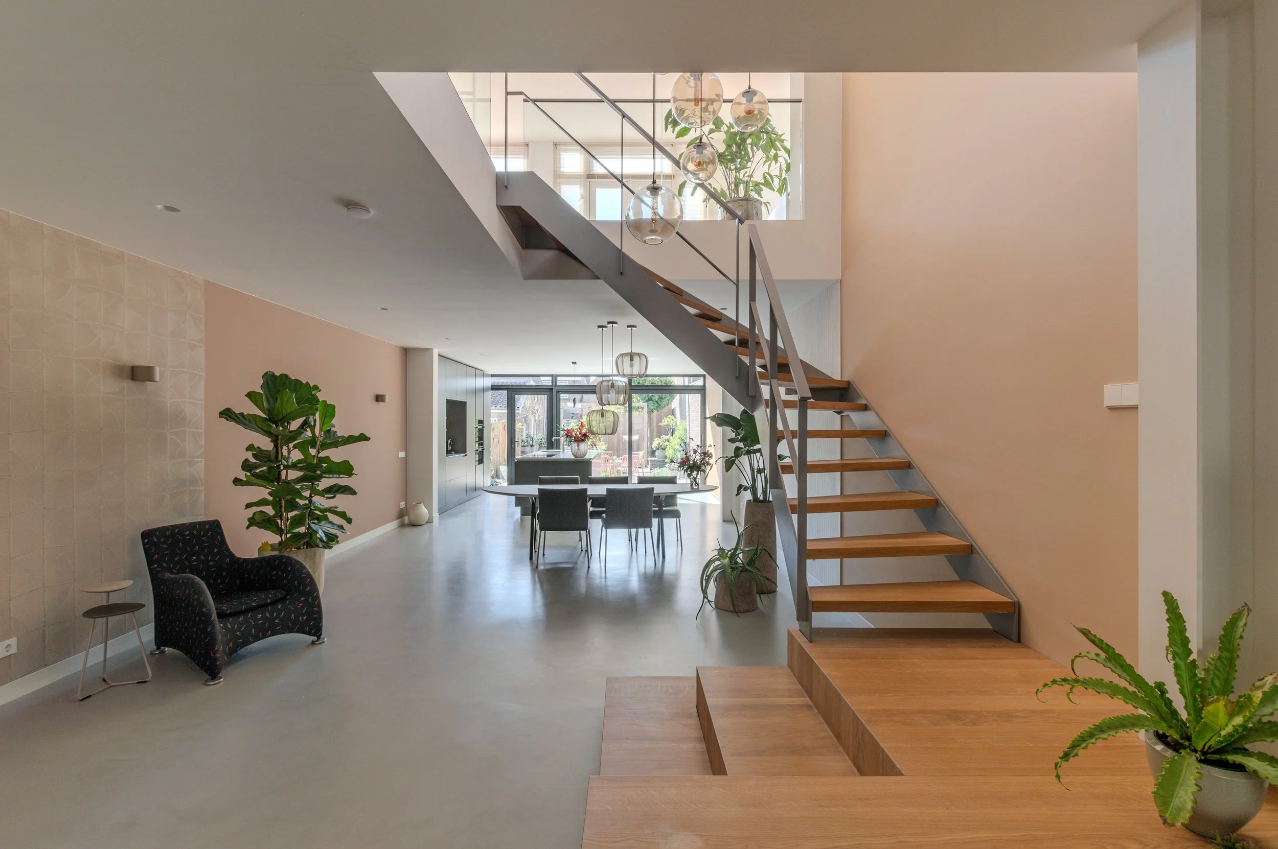 modern strak interieur met een mooie trap in een vide met zicht op de tuin. Woonkamer en keuken op de begane grond. Gietvloer en lichtroze wanden