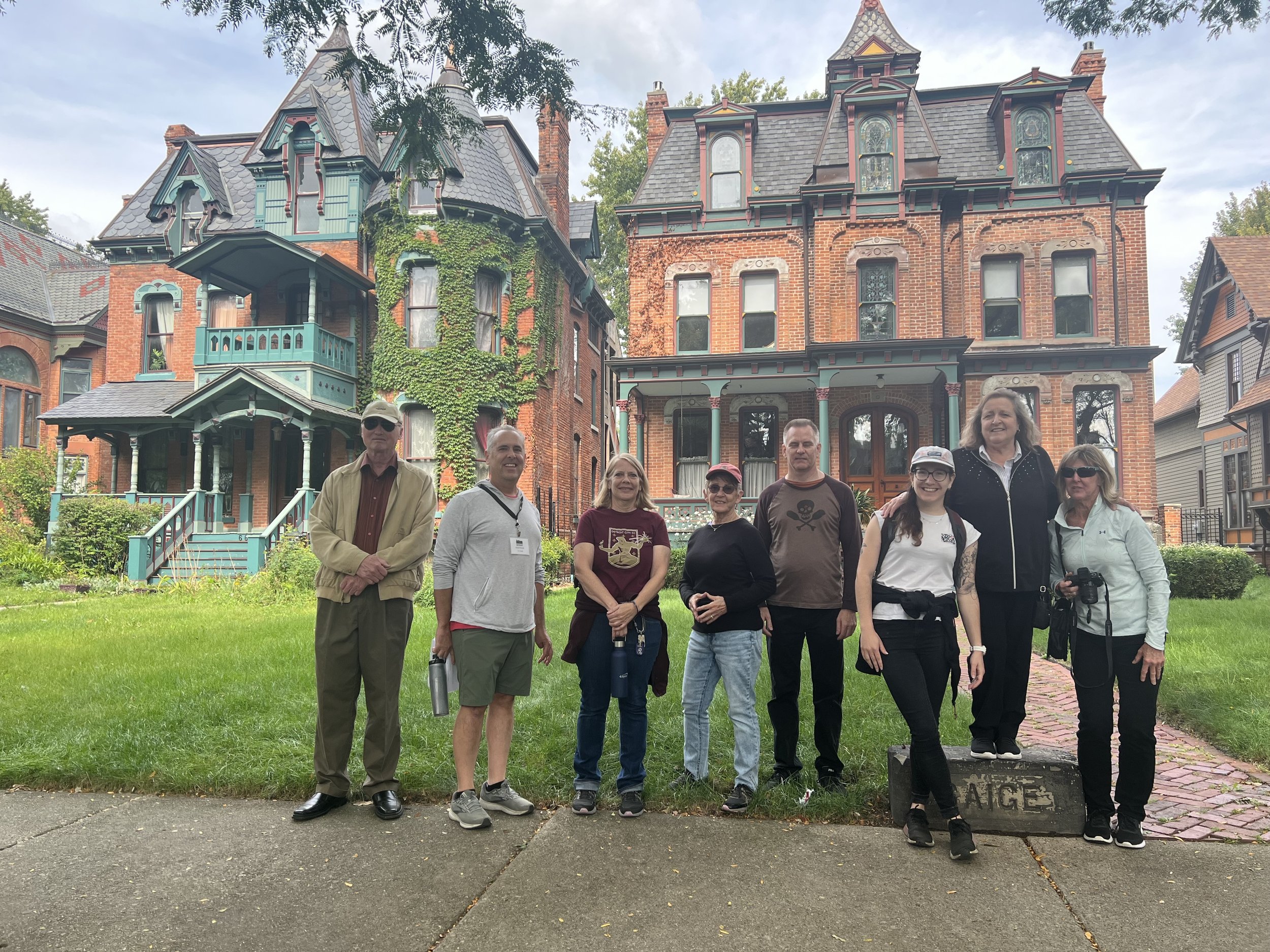 A tour group smiles and stands on the sidewalk in front of a row of historic brick homes on Canfield Street.