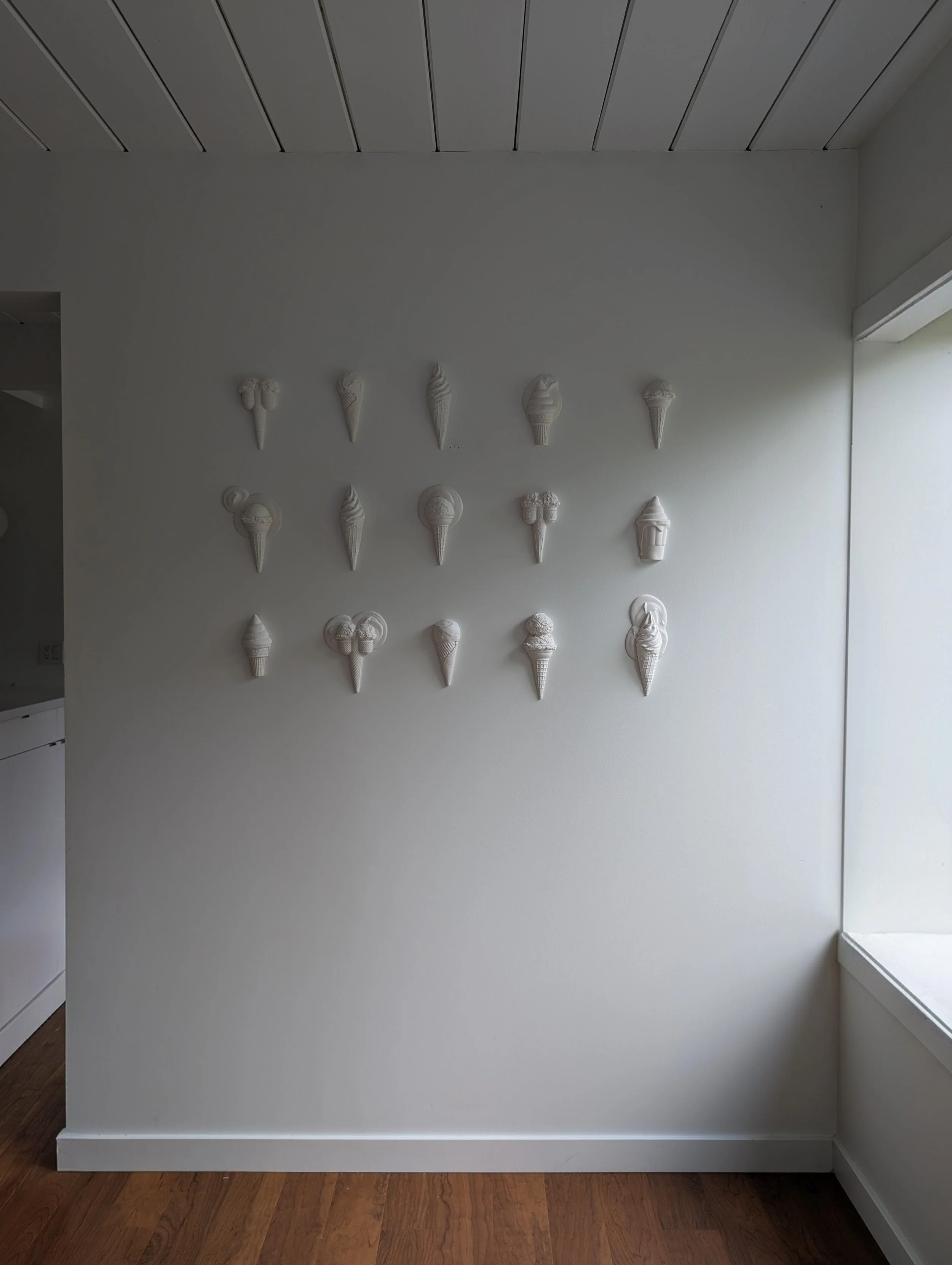 Gallery wall of white sculptural ice cream artwork arranged in rows.