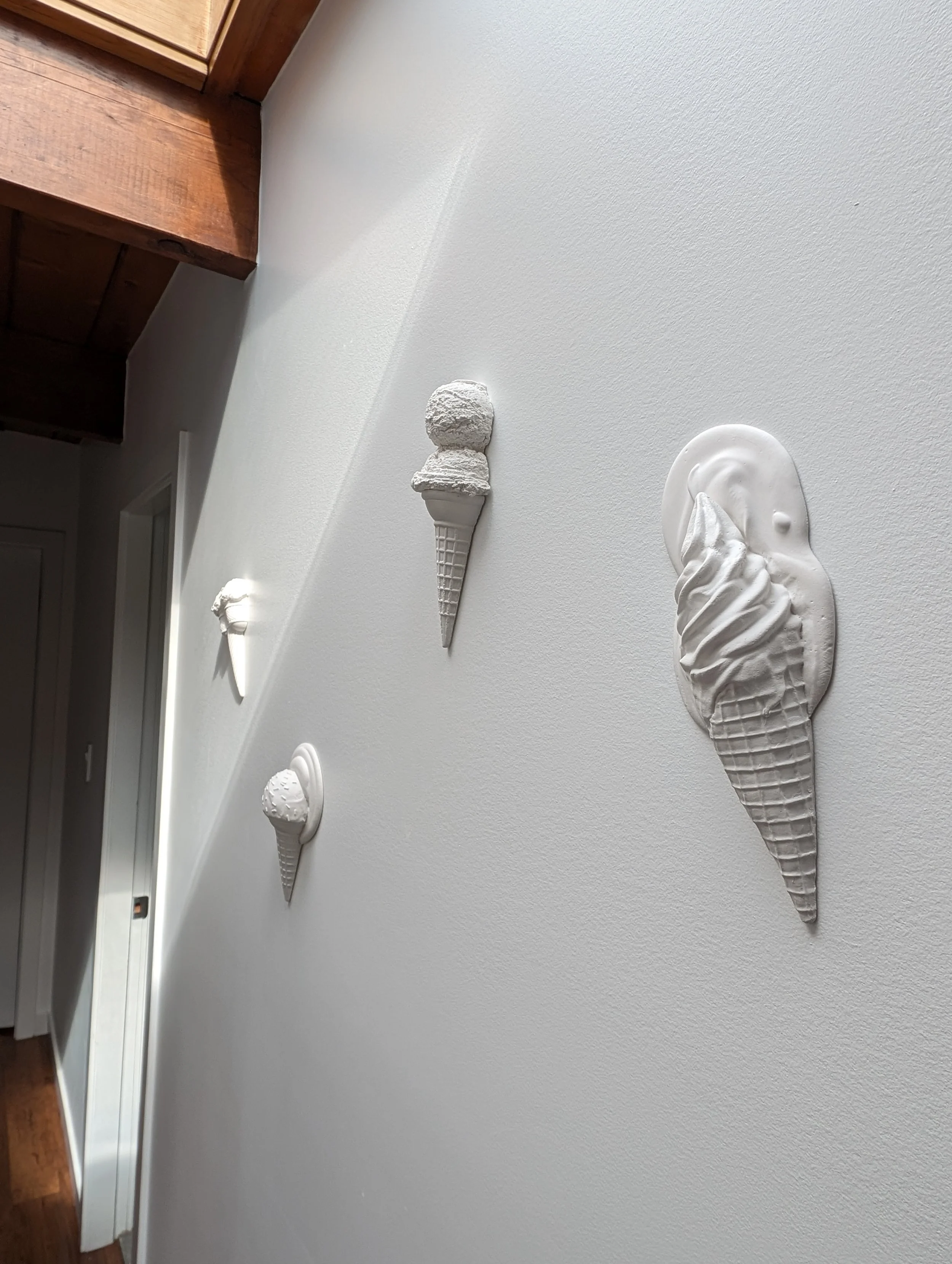Wabi-sabi wall-mounted ice cream sculptures in a bright hallway with a minimalist vibe.