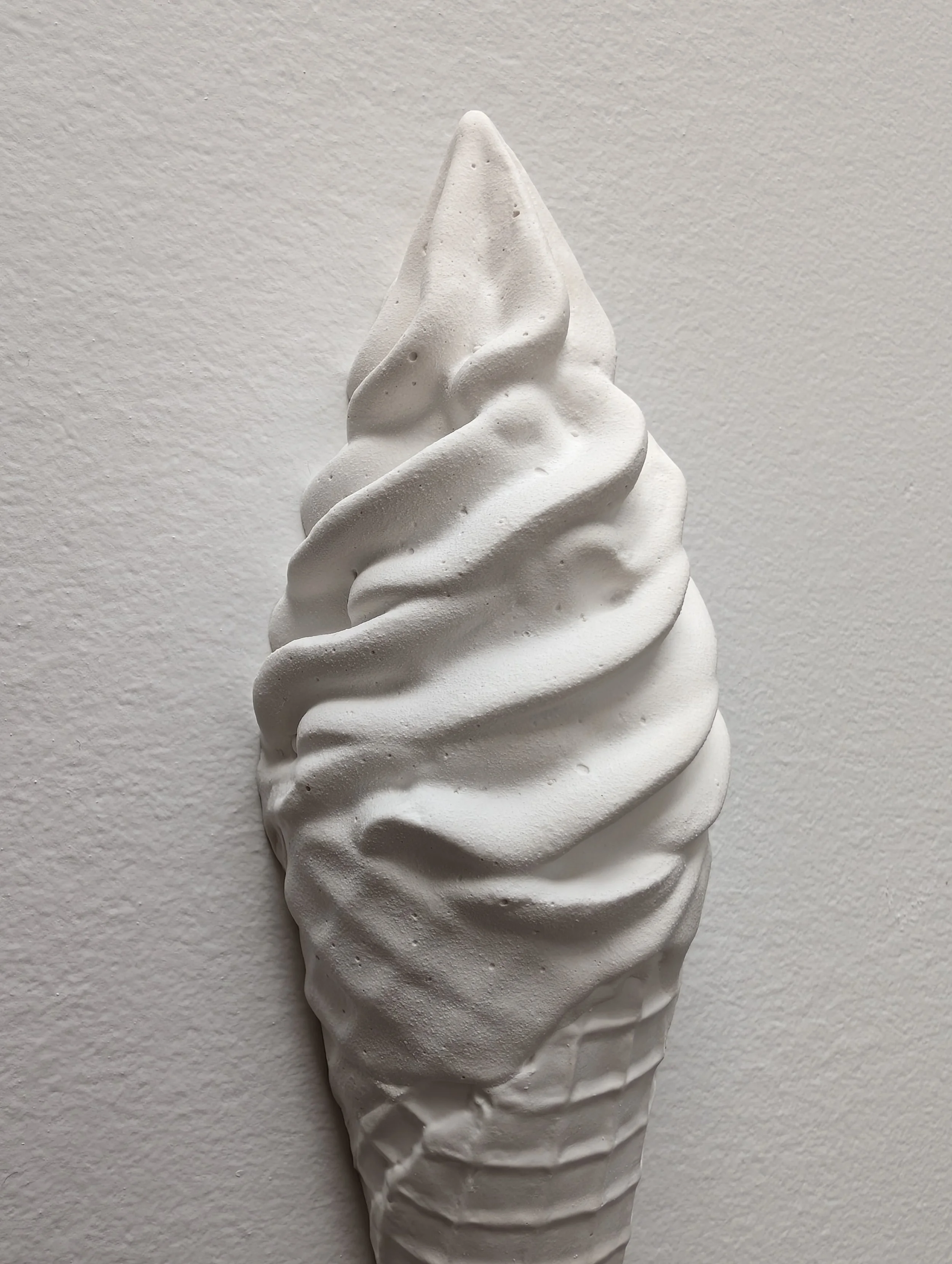 Close-up view of a white wall-mounted sculptural ice cream artwork, showing intricate texture and details, including shadows and highlights.