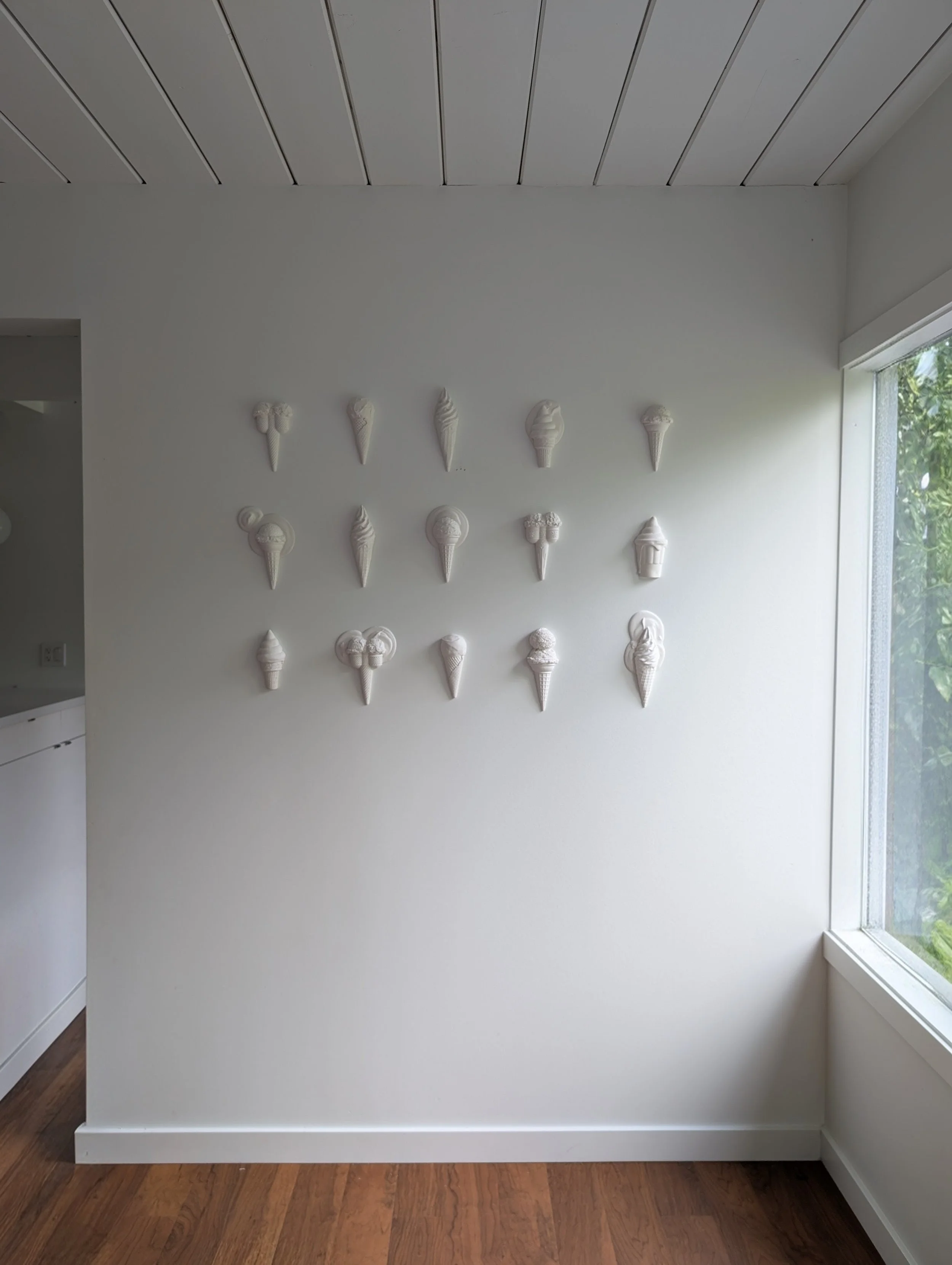 Gallery wall of minimalist, white wall sculptures of ice creams arranged in a geometric pattern. Created by artist Lindsay Cohen in Vancouver, Canada.