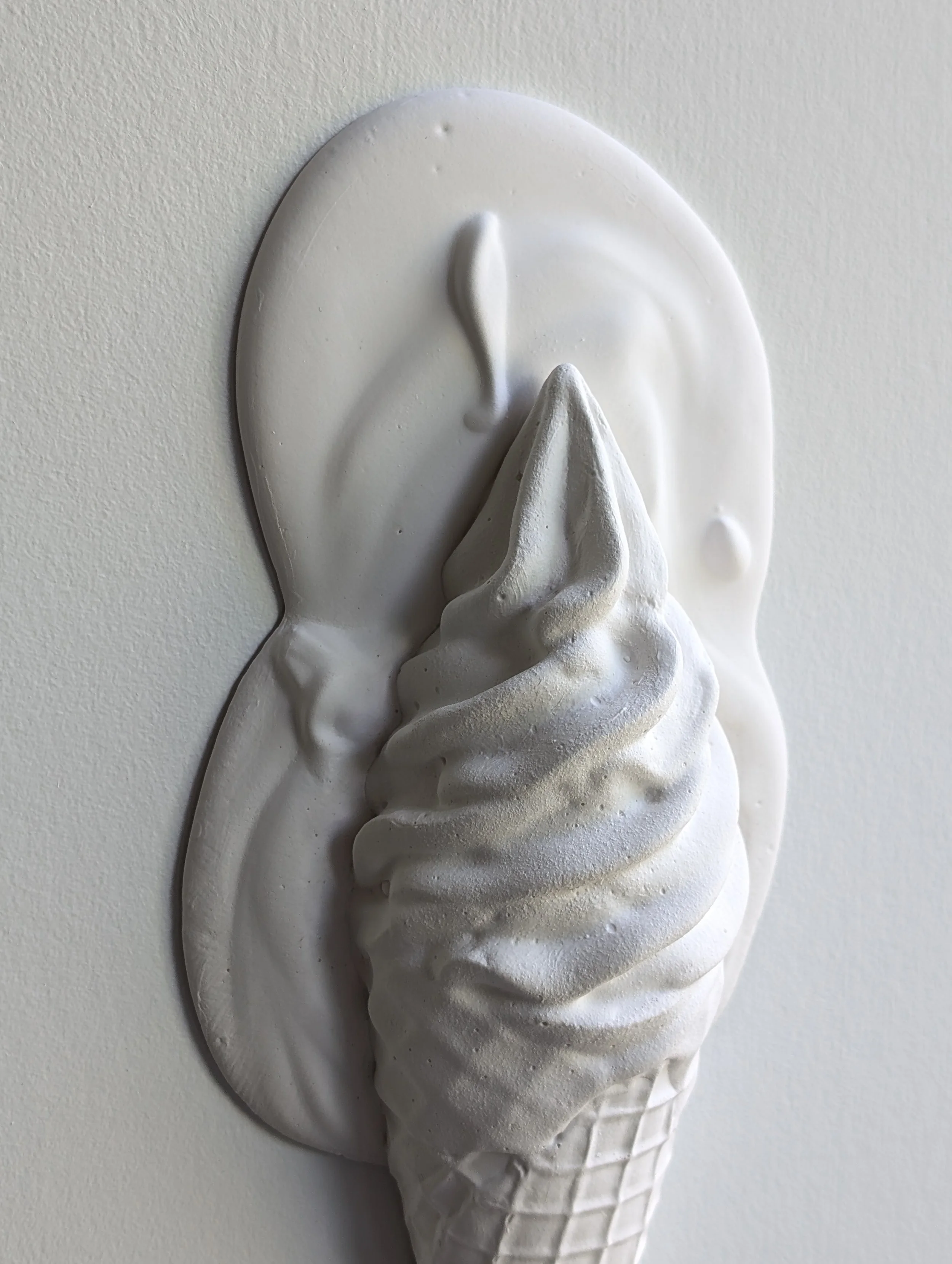 Melting soft serve scoop, an all-white sculptural artwork mounted to the wall.