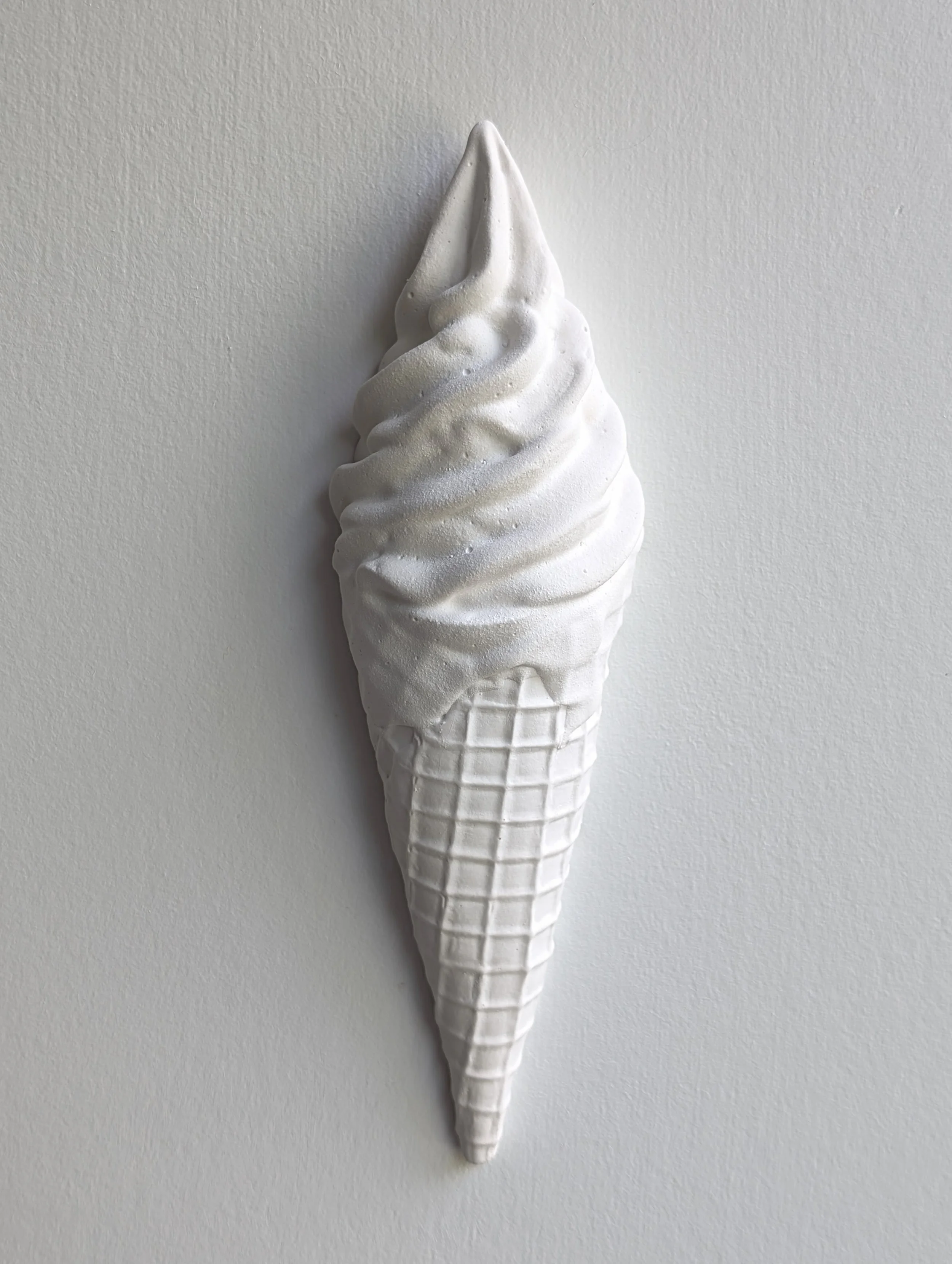 Details of an all-white wall-mounted ice cream artwork, featuring a waffle cone and soft serve. Sculpture created by Lindsay Cohen in Vancouver, Canada.