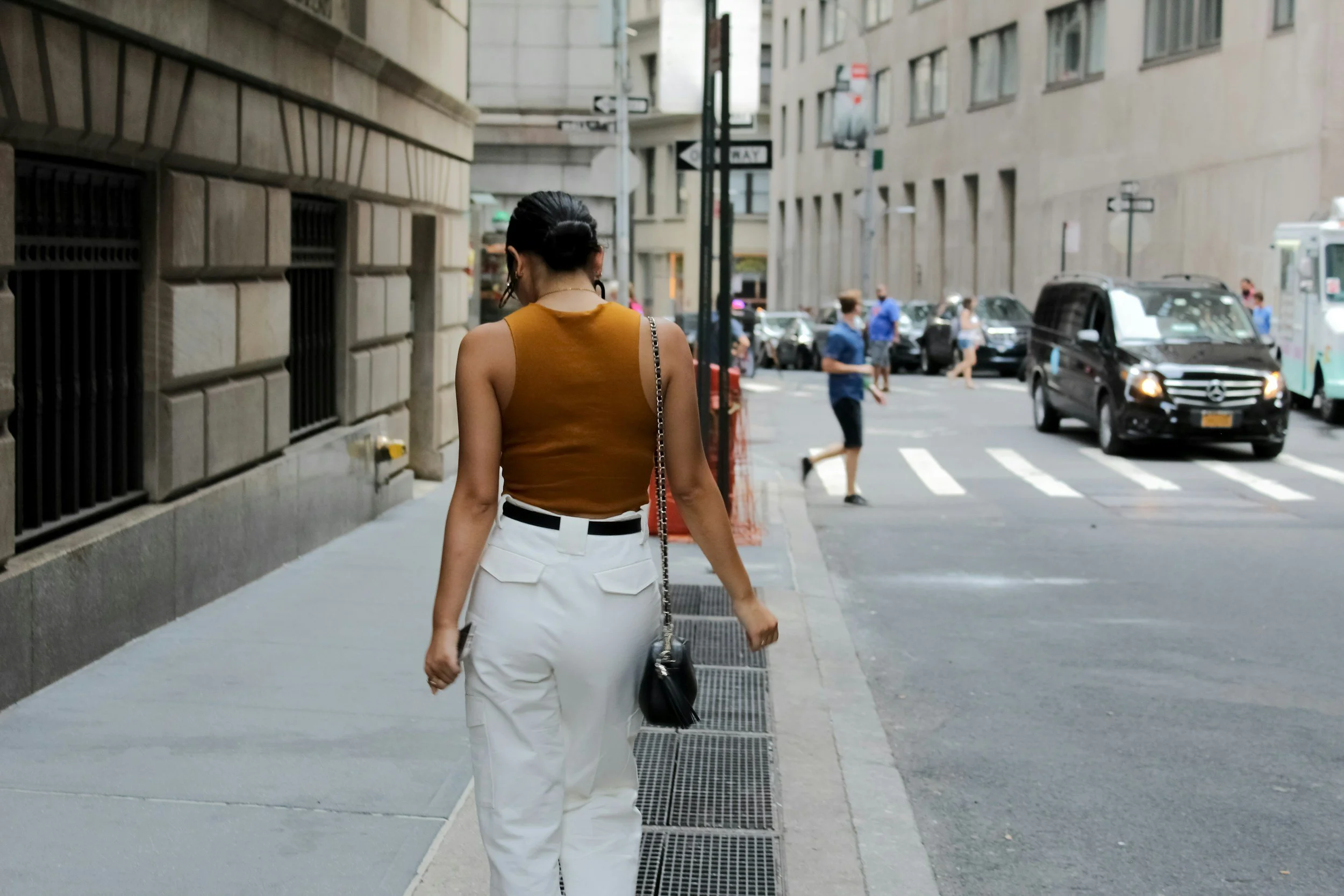 woman wearing white pants and burnt orange sleeveless top walks down NYC street