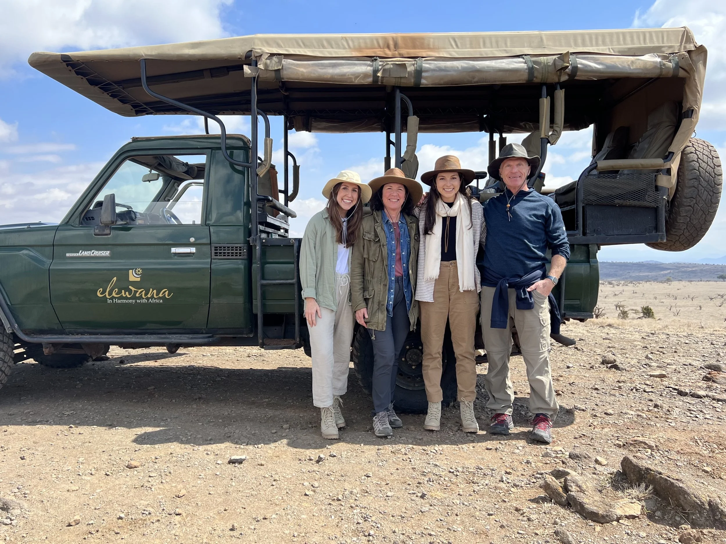 family of four stands in the desert in front of a safari truck
