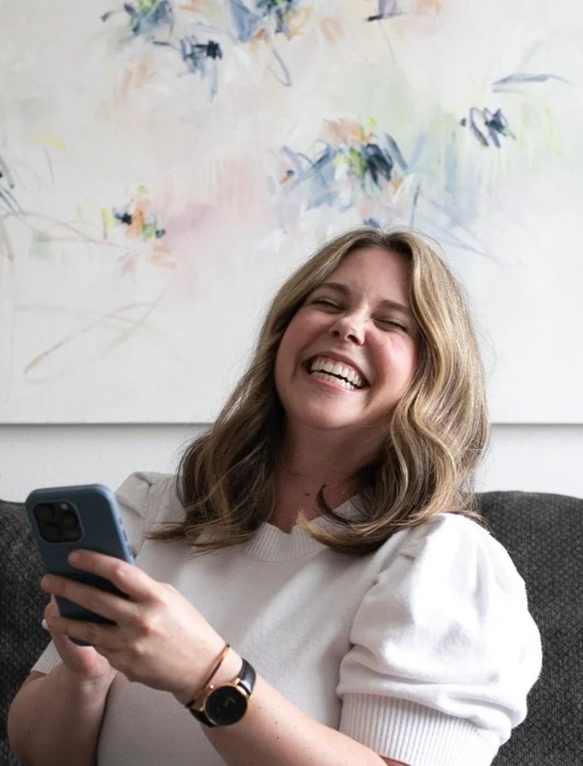 Nicole Bissett laughing indoors while holding an iPhone