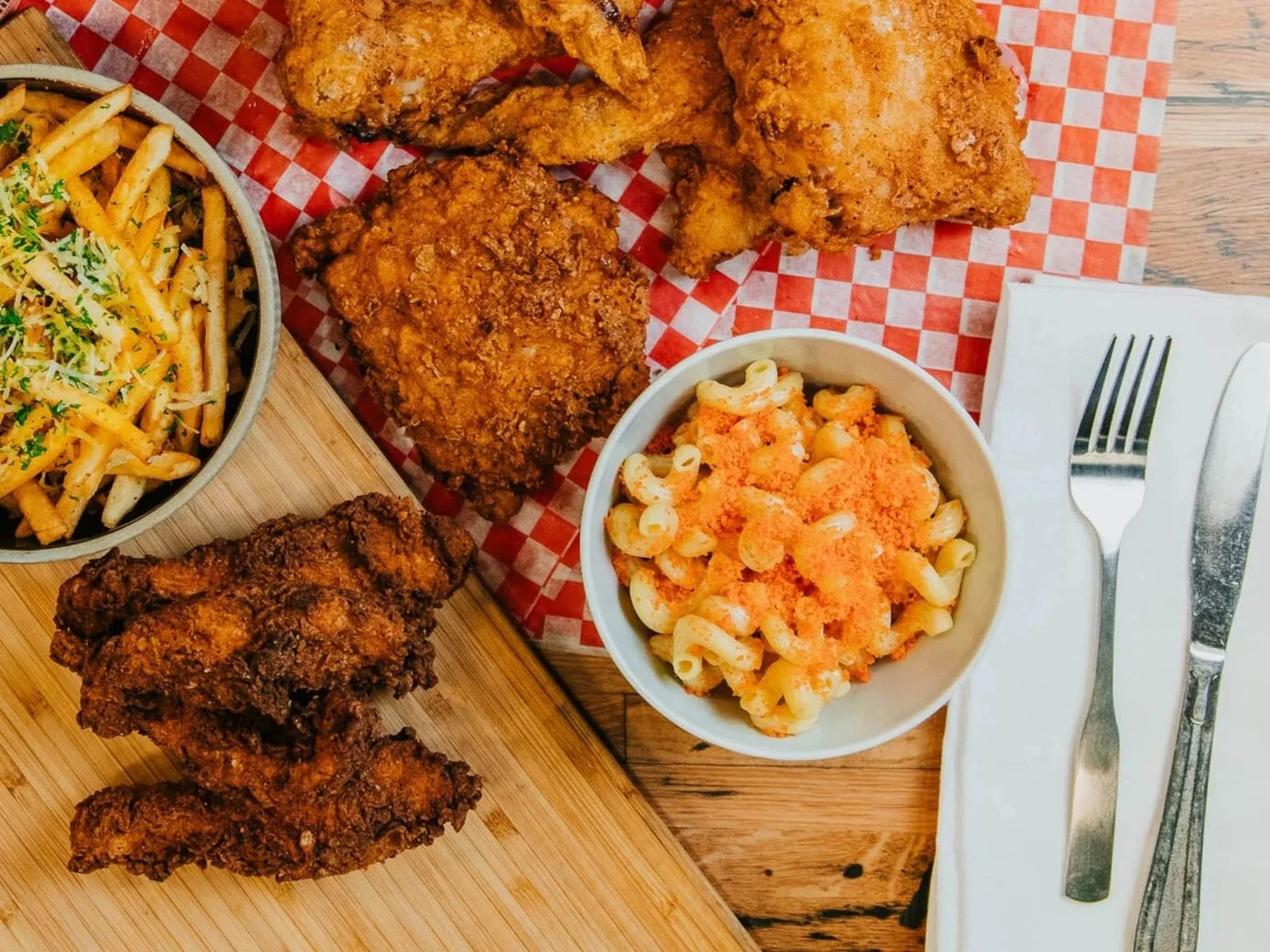 Fried chicken served with macaroni and cheese, French fries, and dipping sauces on a wooden table.