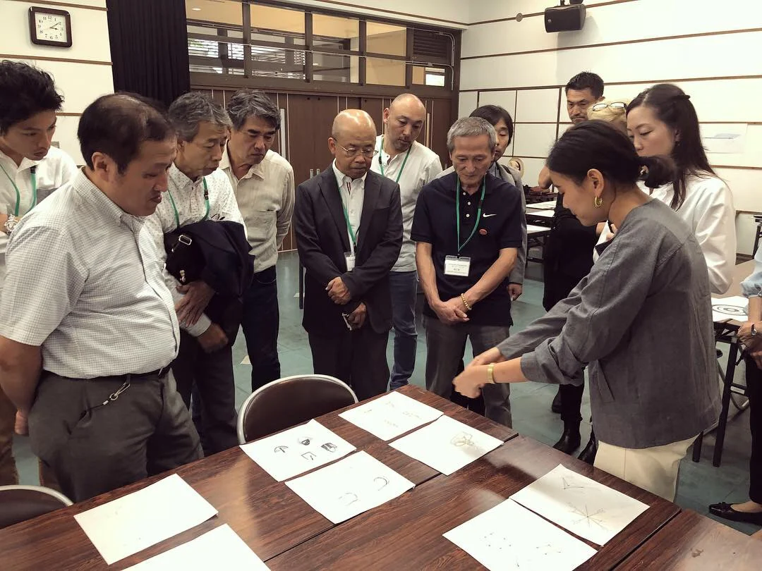  A group of Japanese men huddled around a designer to see her work 