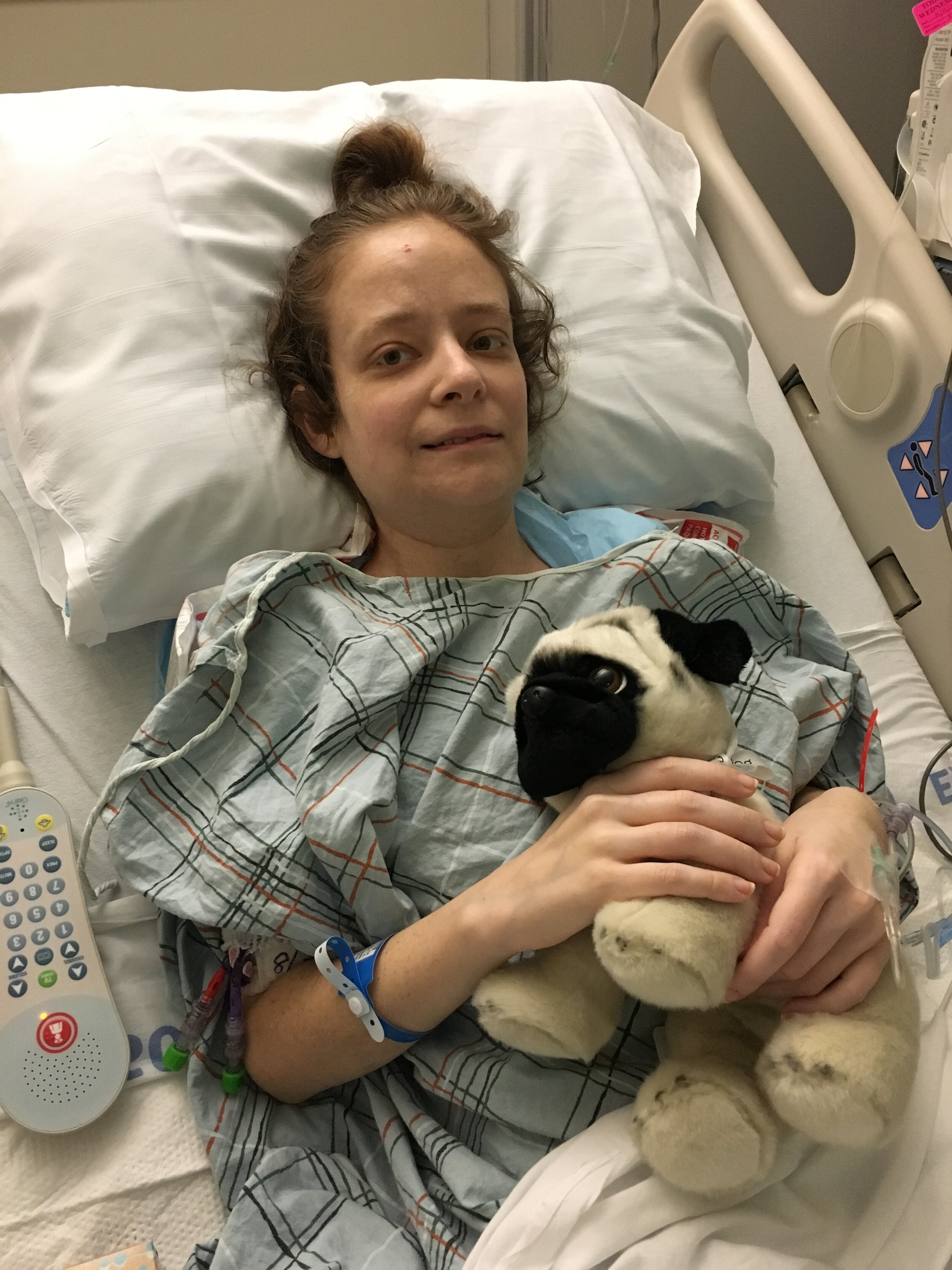 The blogger sits in a hospital bed holding a stuffed pug.
