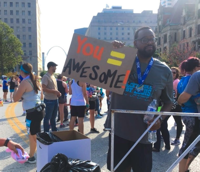 An image of the author’s husband Reggie cheering Taryn on as she crossed finish line at a race in St. Louis holding a sign that says, “you = awesome.”