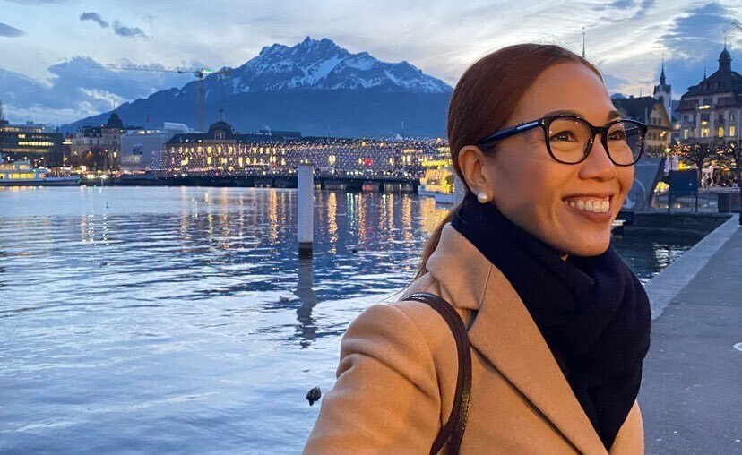 An image of the blog author outside by the water with a view of a building and mountain.