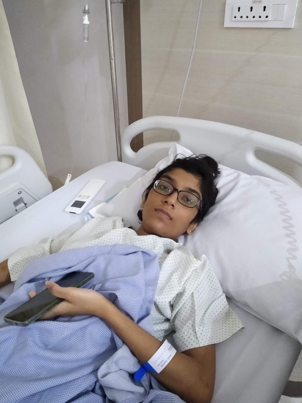 Image of Madhura laying in a hospital bed recuperating after an emergency hospitalization in the middle of the national lockdown.