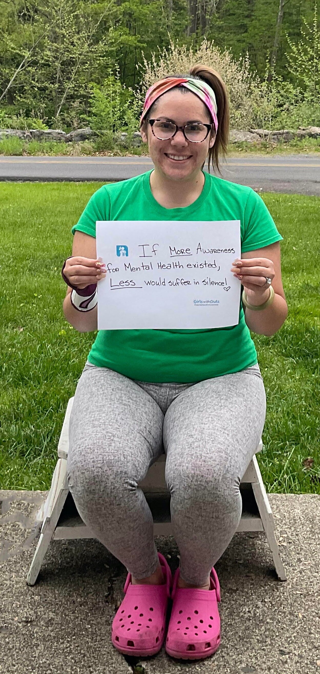 Image of a woman (Nina) outside holding a sign that says, "If more awareness for mental health existed, less would suffer in silence!"