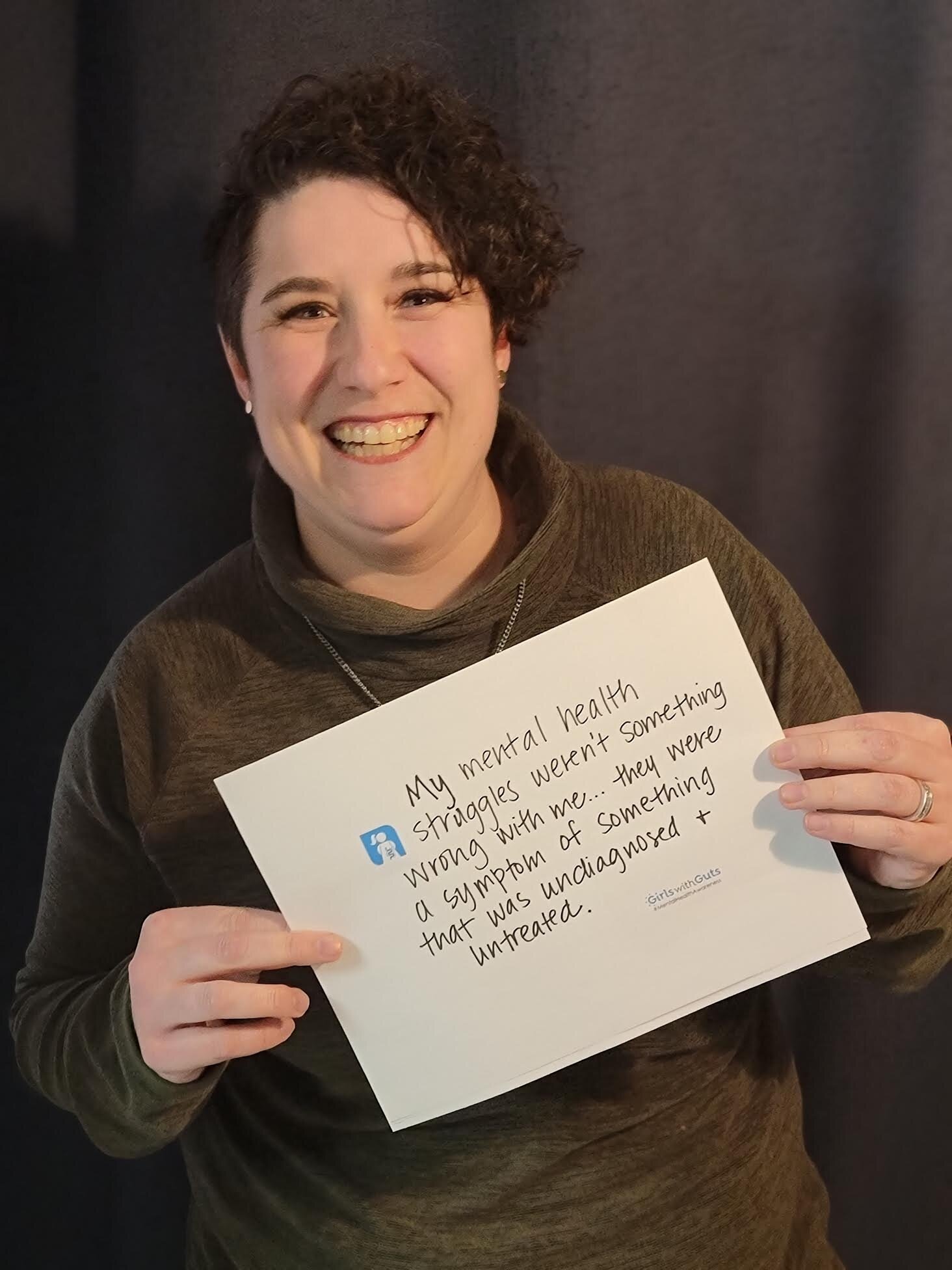 Image of a woman (Charlotte) in front of a black backdrop holding a sign that says, "My mental health struggles weren't something wrong with me...they were a symptom of something that was undiagnosed and untreated."