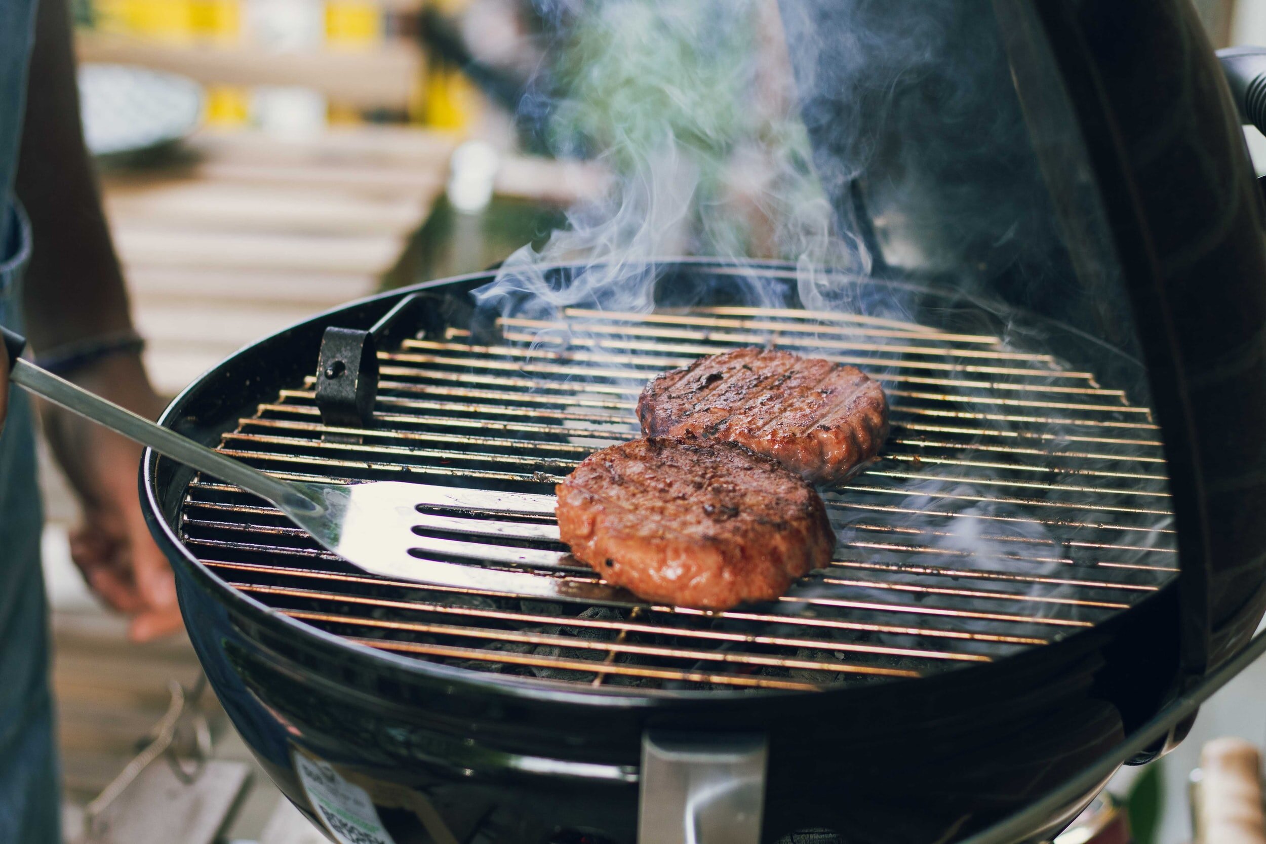 Image of two brugers being cooked on a small black charcoal grill. Photo by Maude Frédérique Lavoie on Unsplash