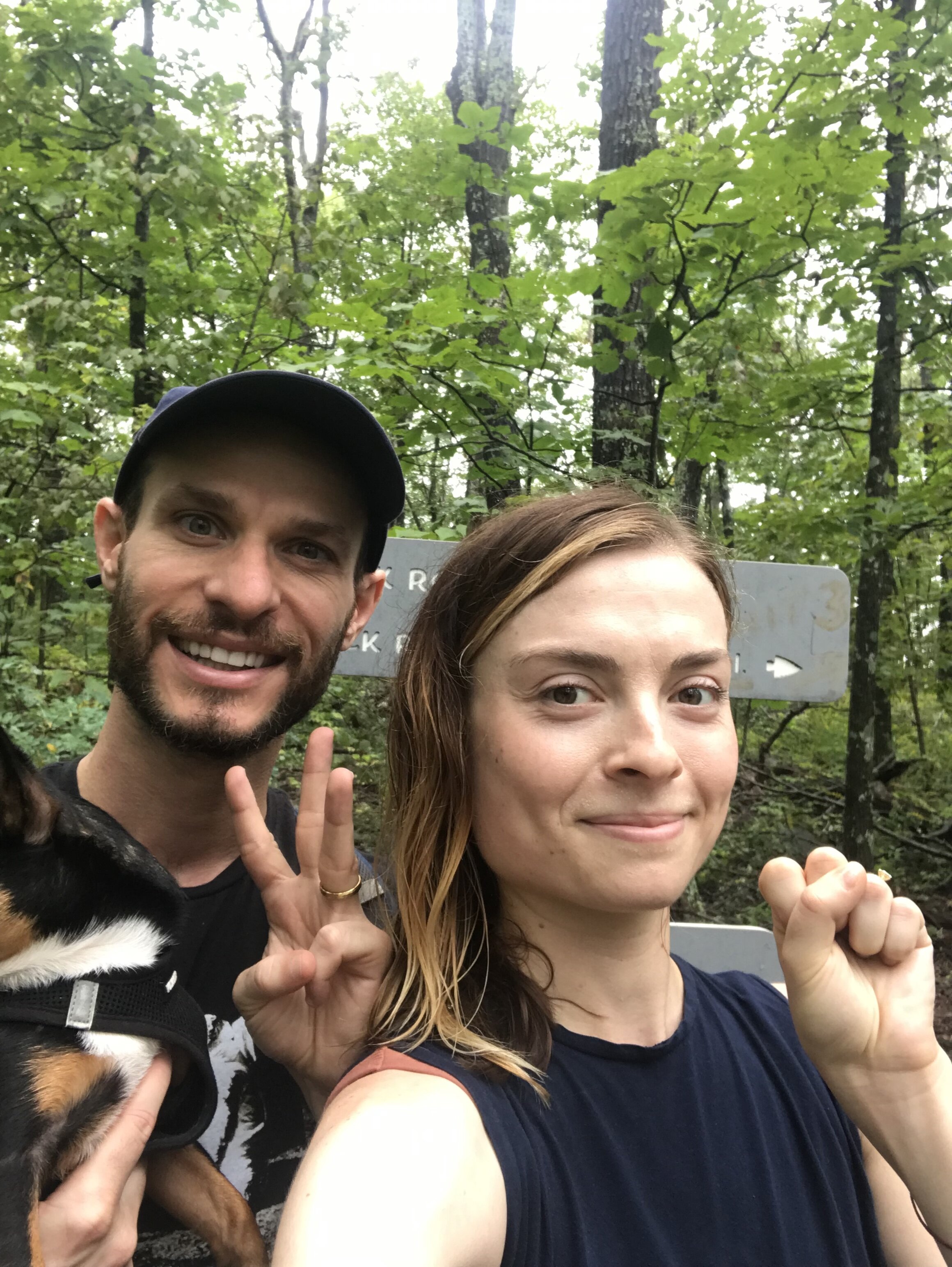 Photo of the author hiking with her husband. There are green trees and a trail sign behind them.