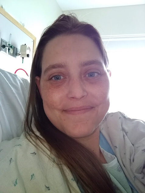 An image of the blog author a woman with brown hair in a hospital gown sitting upright in a hospital bed.